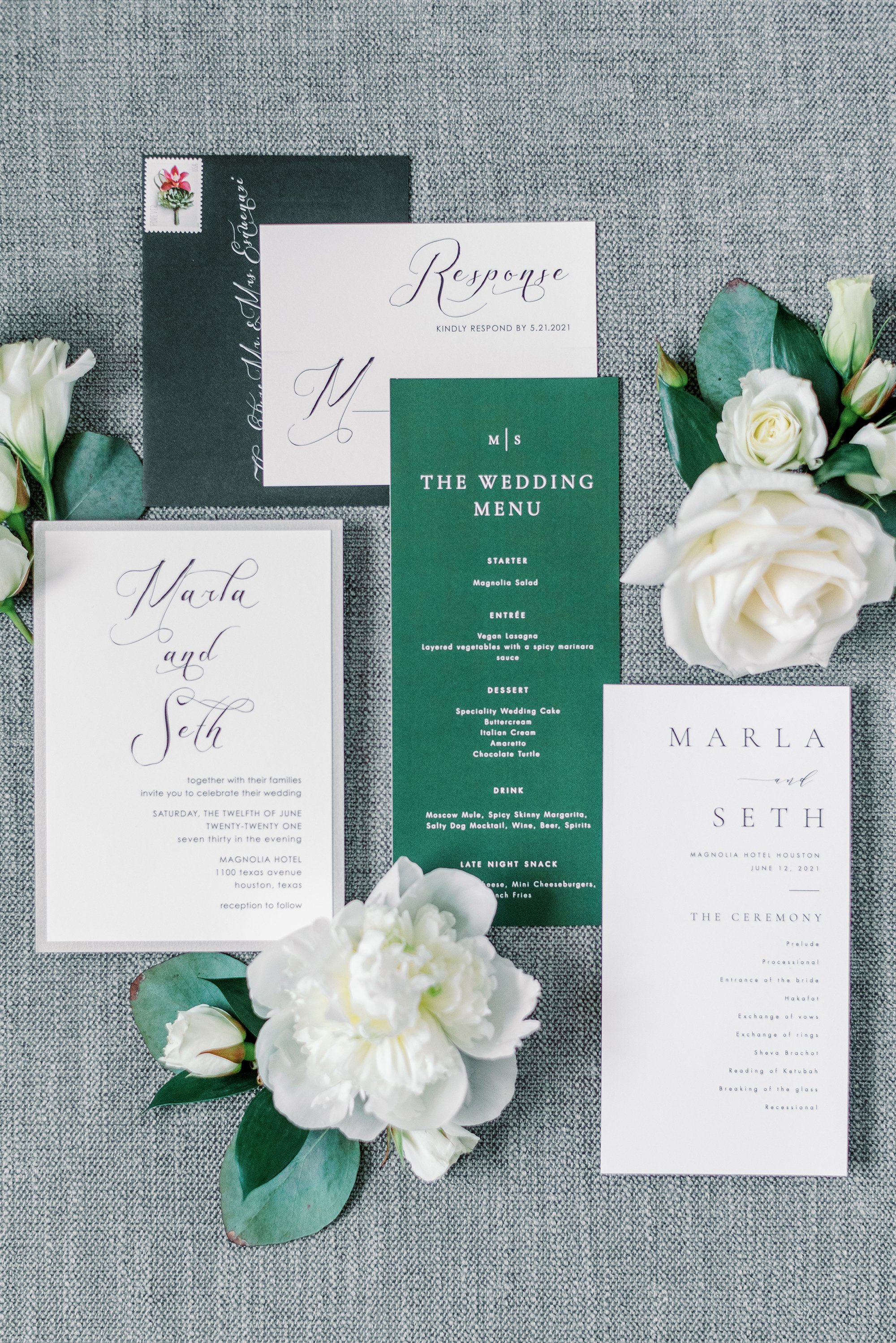 A photography flat lay with the bride and groom's wedding invitation, menu and envelope in green, black and white. The flat lay also has classic flowers bordering in including white peonies, white roses and Lisianthus. 