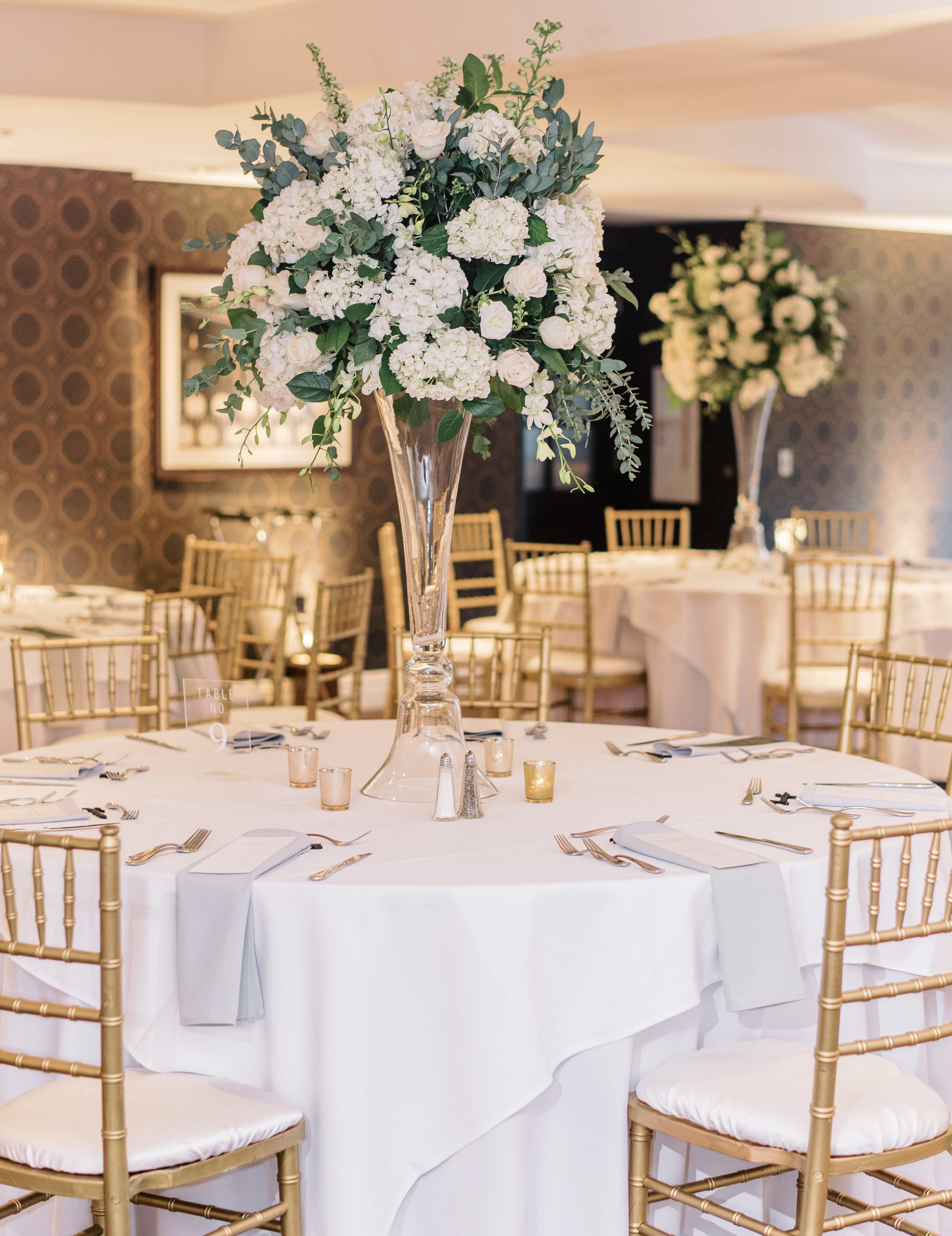 The floral centerpieces are set up in the middle of the tables on classic glass risers with white hydrangea and roses.