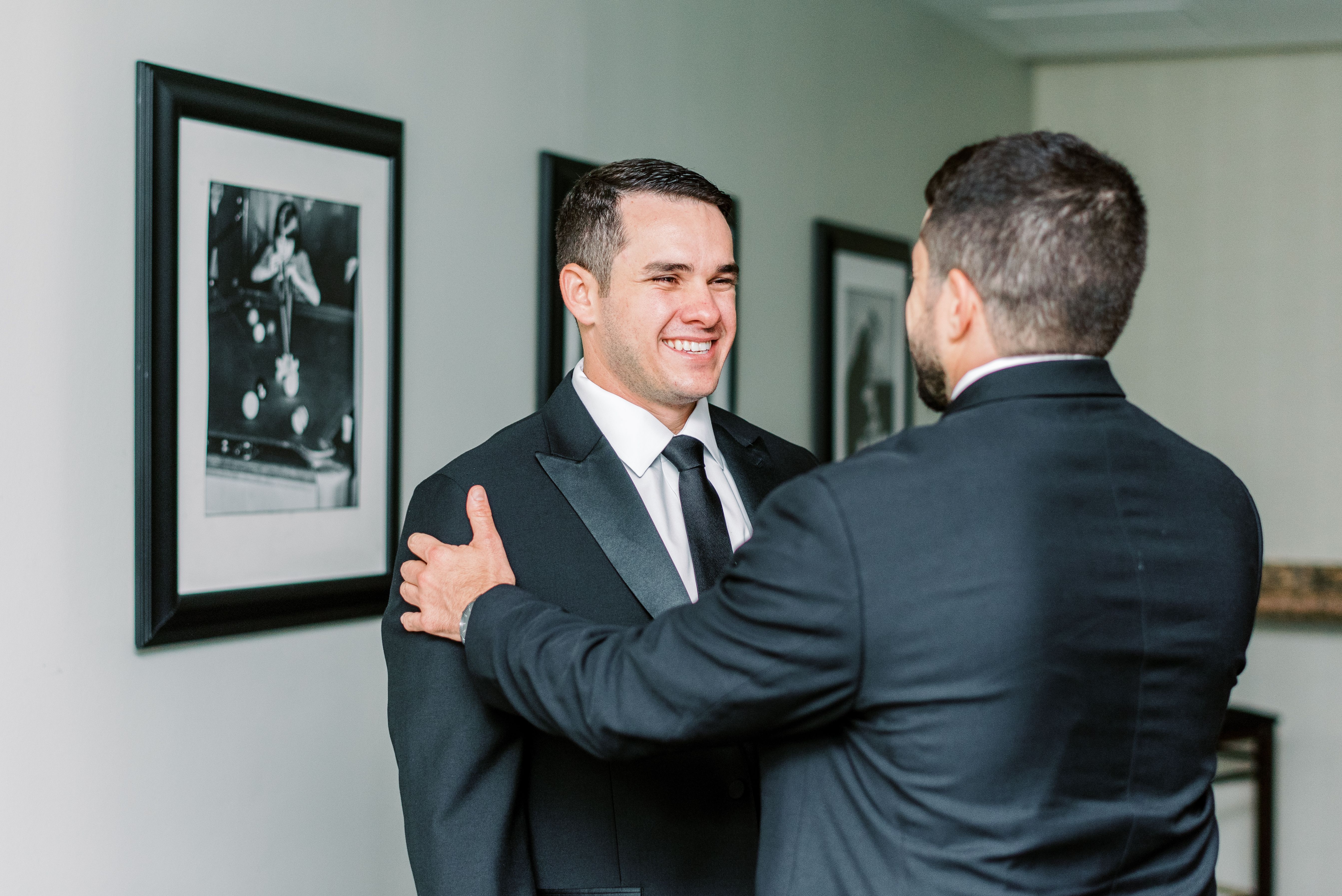 The groom smiles at one of his groomsmen as he grabs his shoulders.