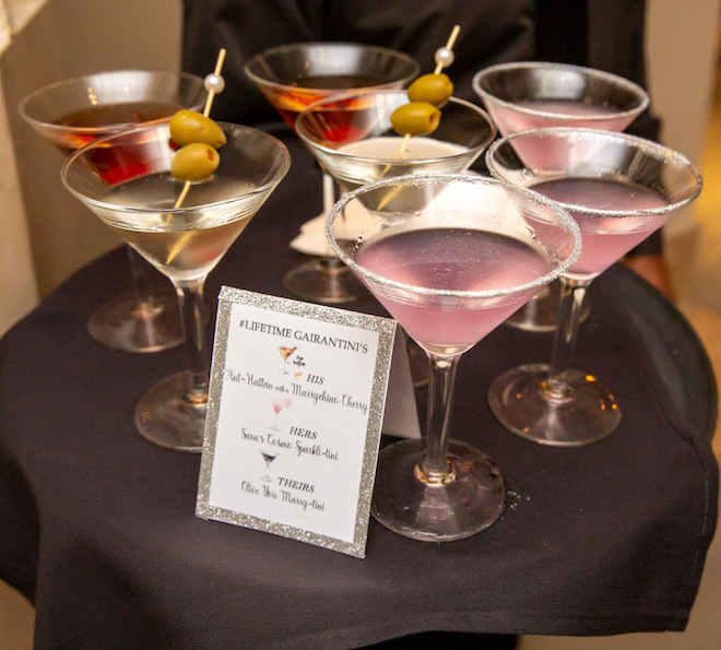 Eight custom light pink and red colored martinis with olives as garnishes. 