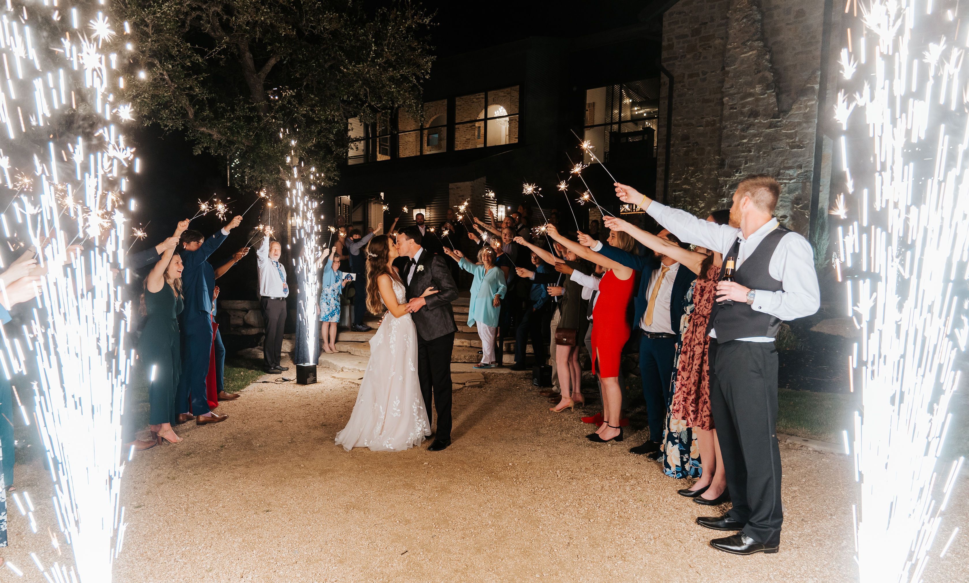 The newlyweds kiss surrounded by sparklers held by their guests, and showering up from the ground.
