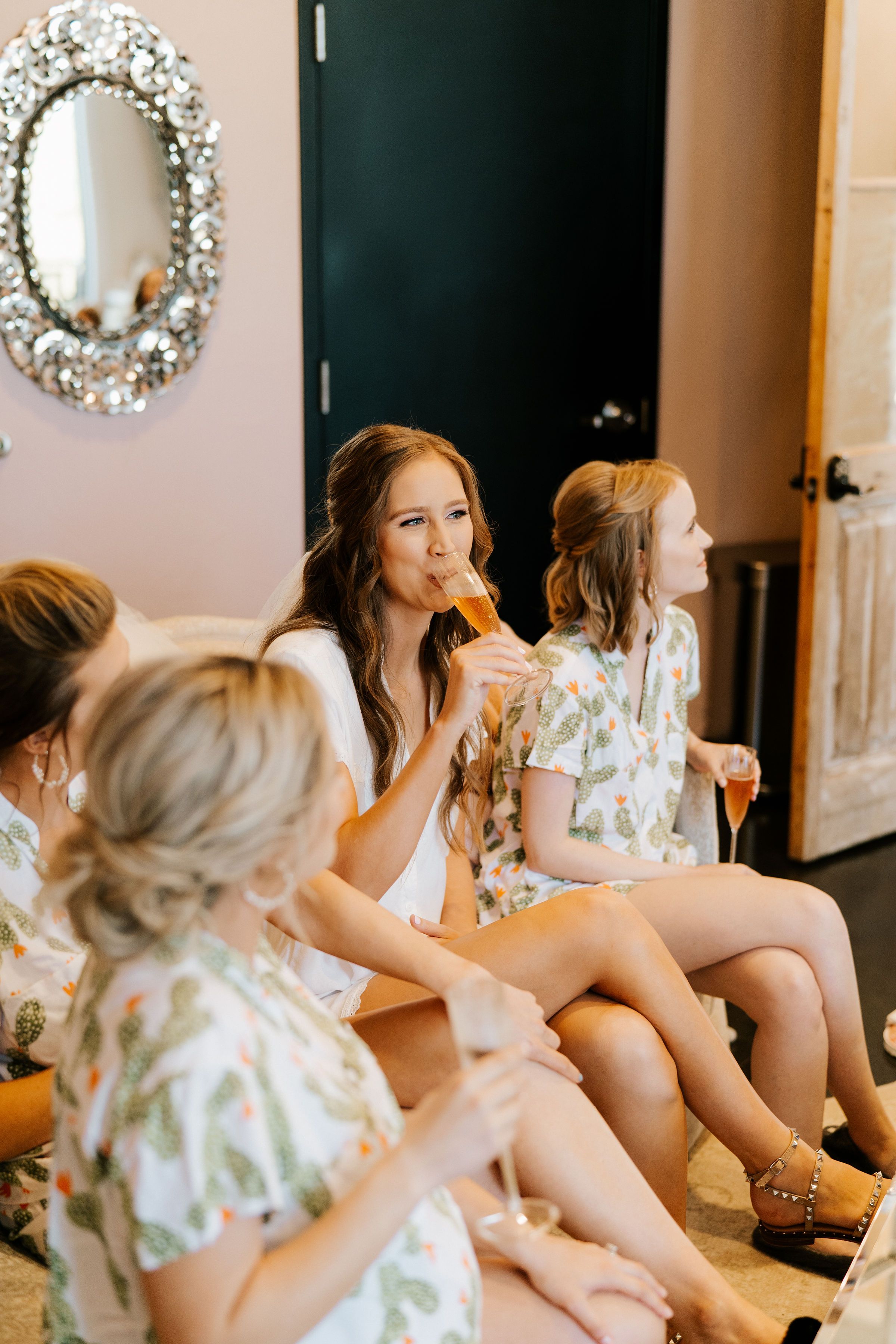A bride to be sips champagne with her bridesmaids while getting ready before the wedding.