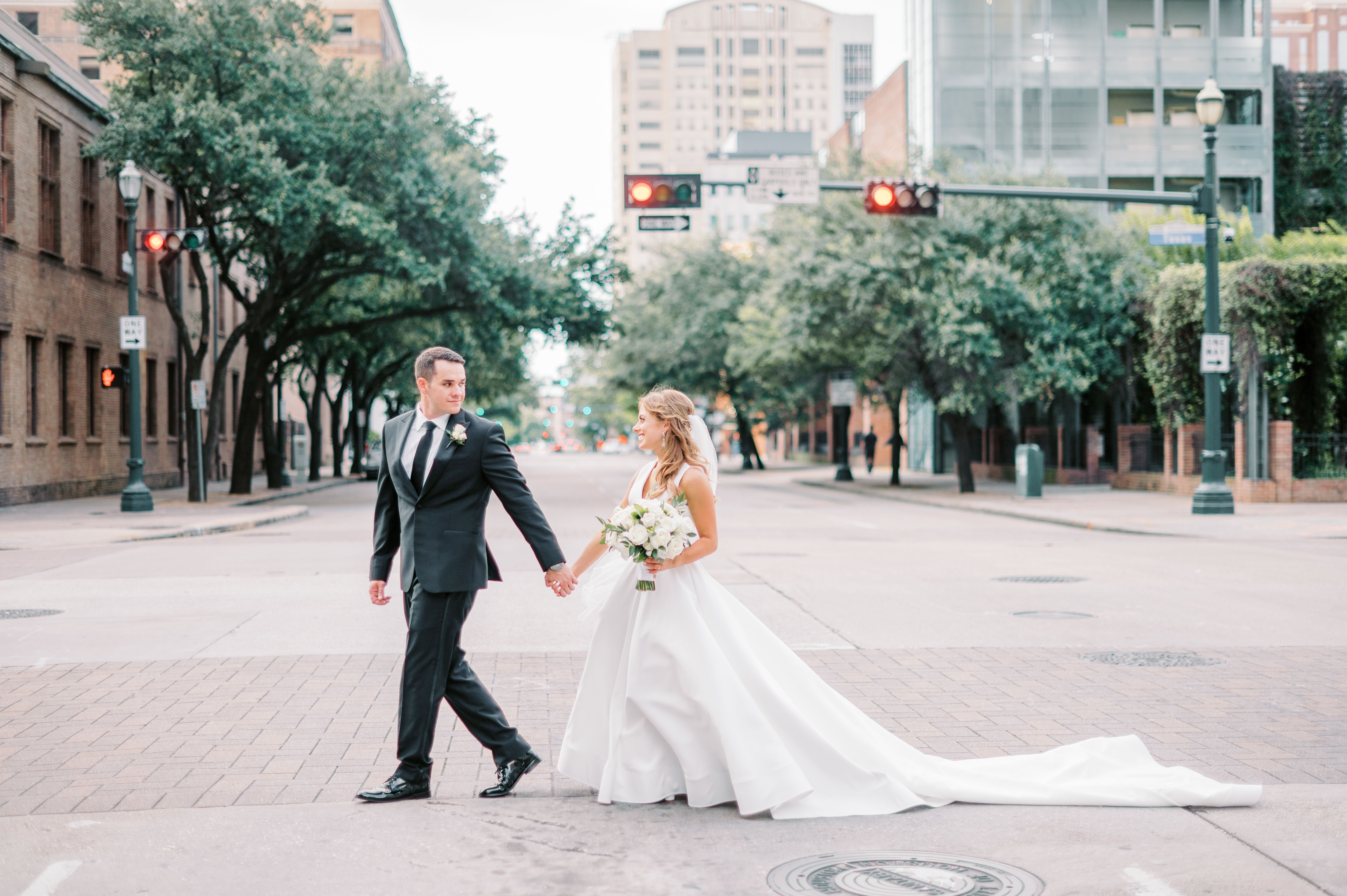 Bride and groom walk across the street in Downtown Houston during the day.