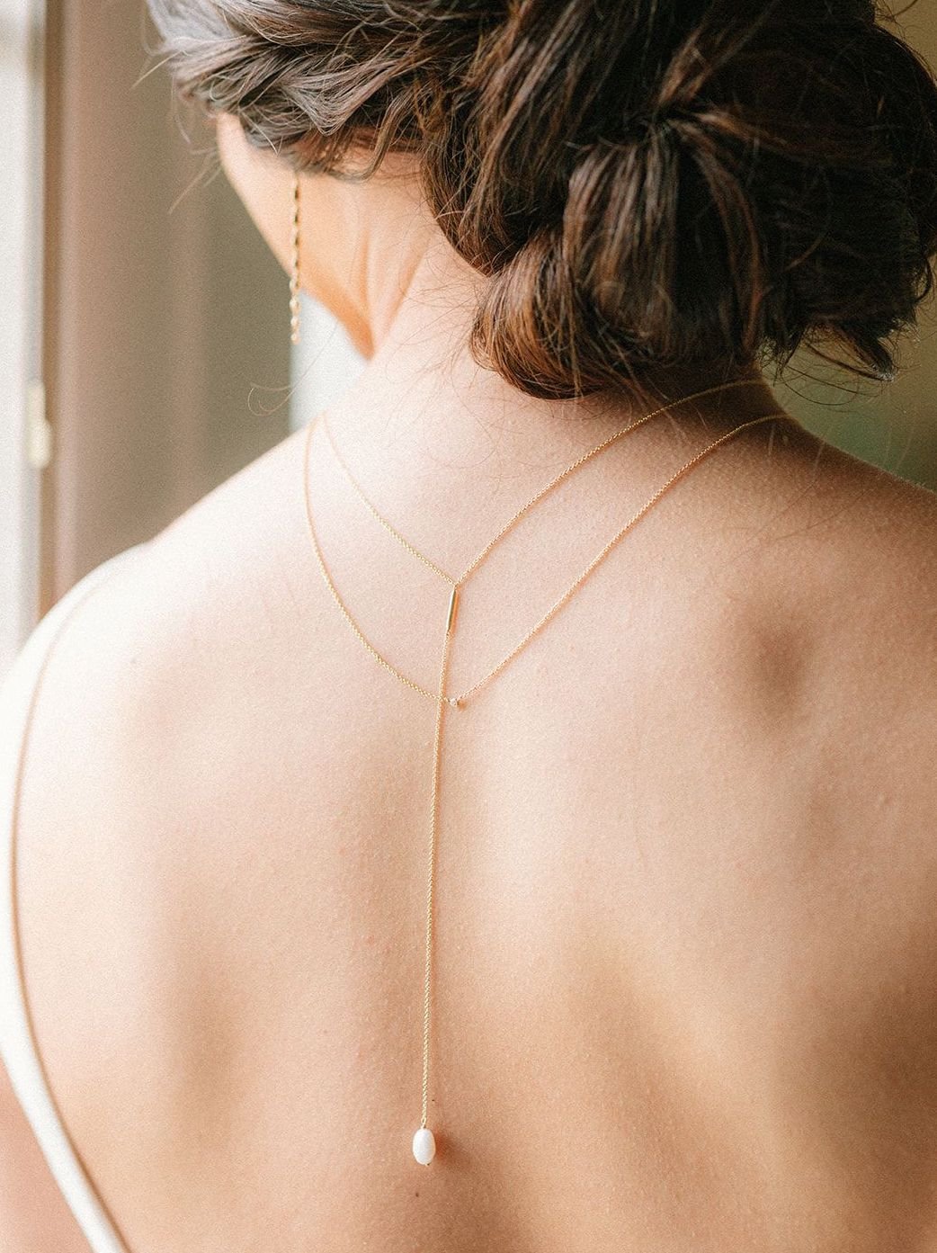 Bride's back is turned to show the pearl backing of her artfully designed necklace for the styled shoot.