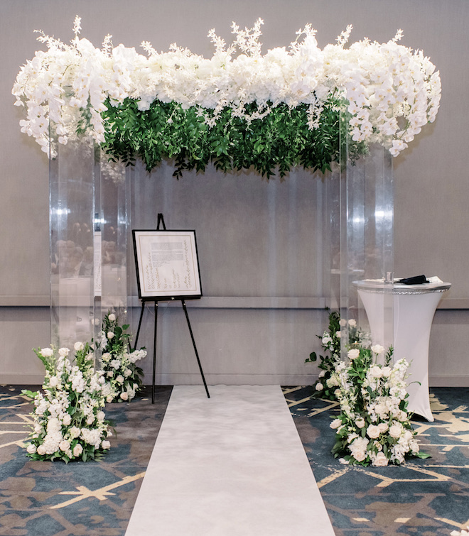 The chuppah is decorated with white orchids and greenery.