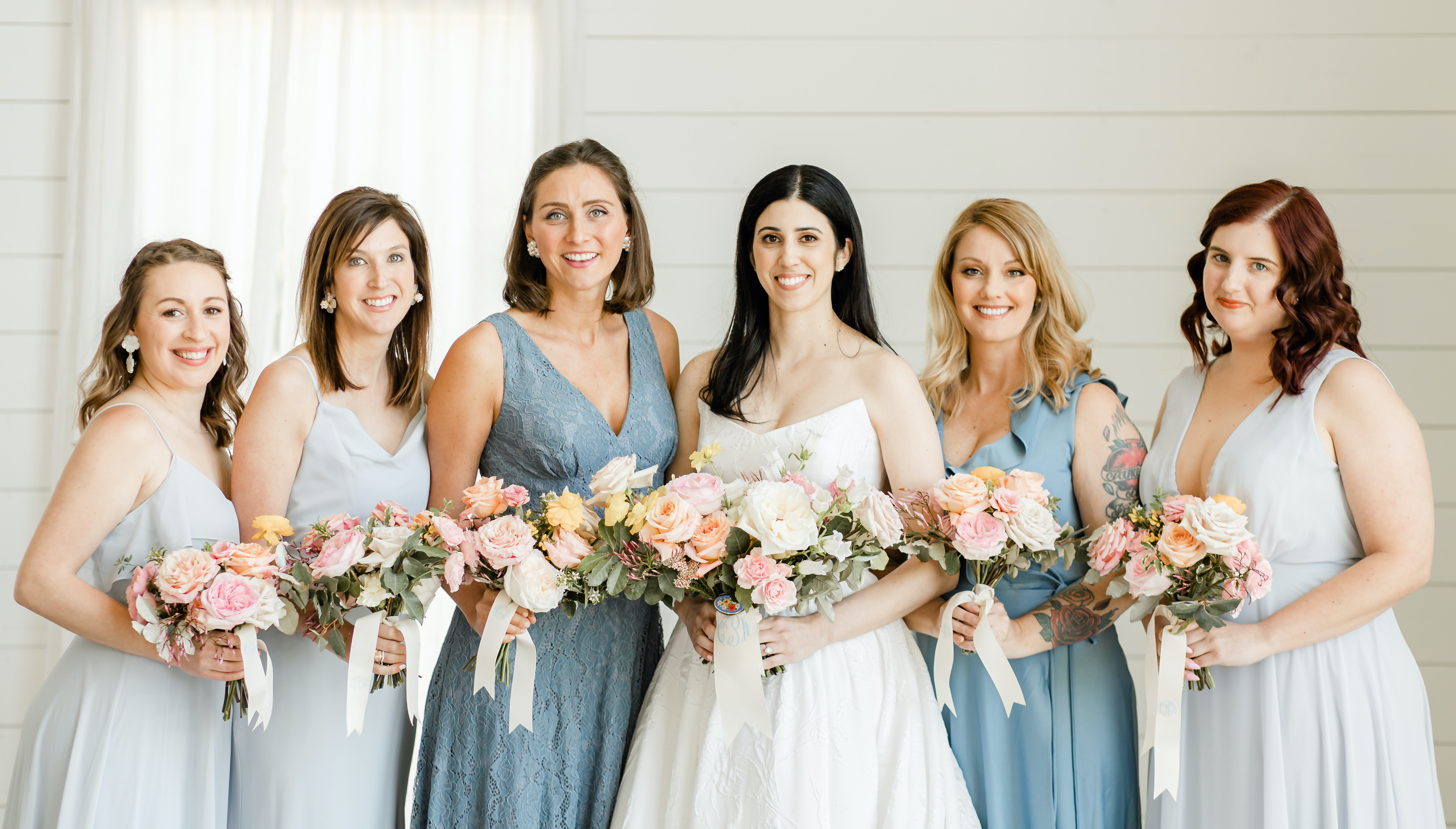 The bride smiles with her bridesmaids and they all hold their colorful bouquets.