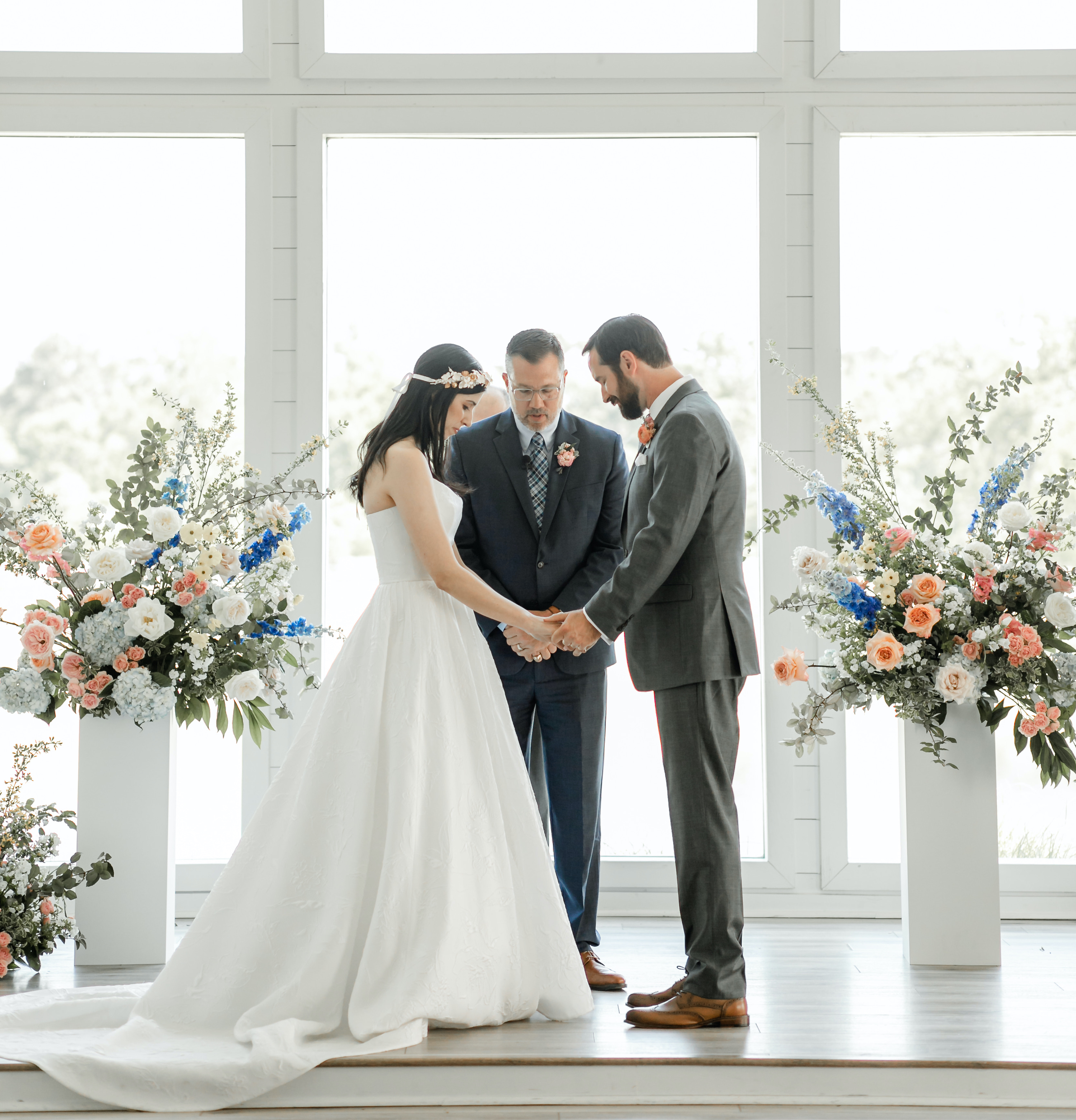 The bride and groom stand at the altar holding hands with flowers surrounding them.