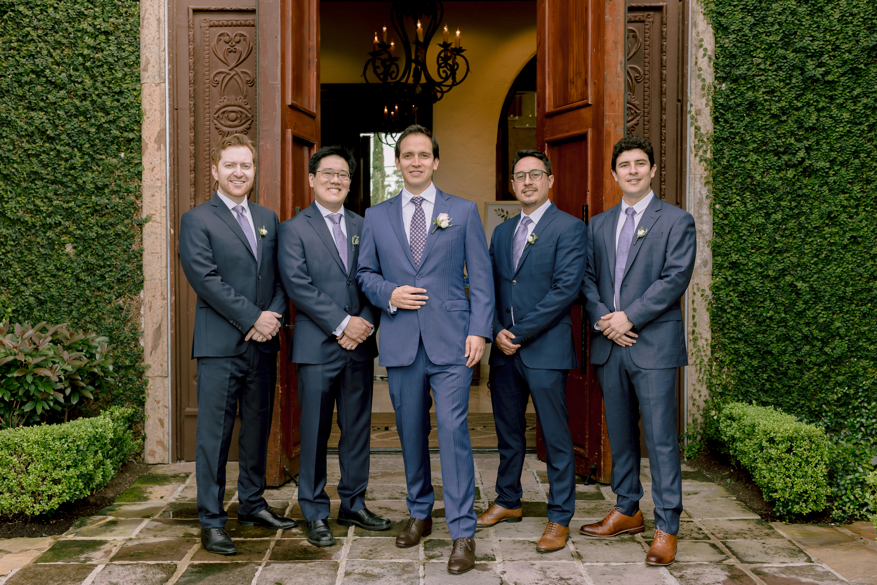 The groom and groomsmen pose in front of the venue entrance.