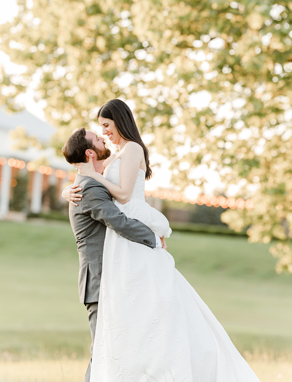 The groom picks up his bride as they smile at one another after their friendly spring wedding.