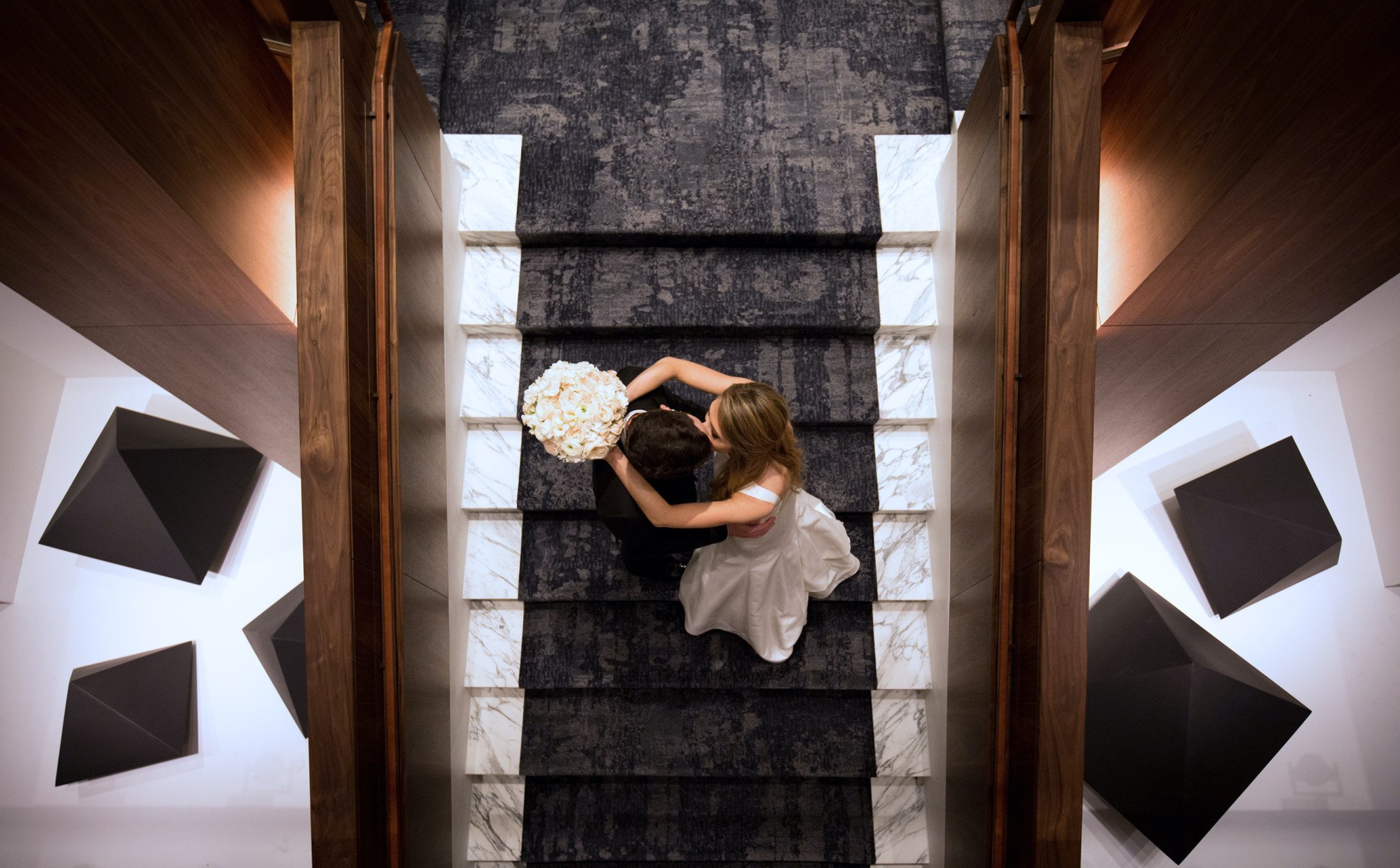 The bouquet holding bride and suited groom kiss each other on the Four Seasons Hotel Houston stairs.