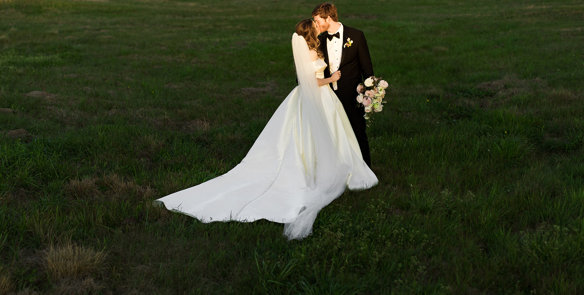 The bride and groom embrace each other in a green open field.