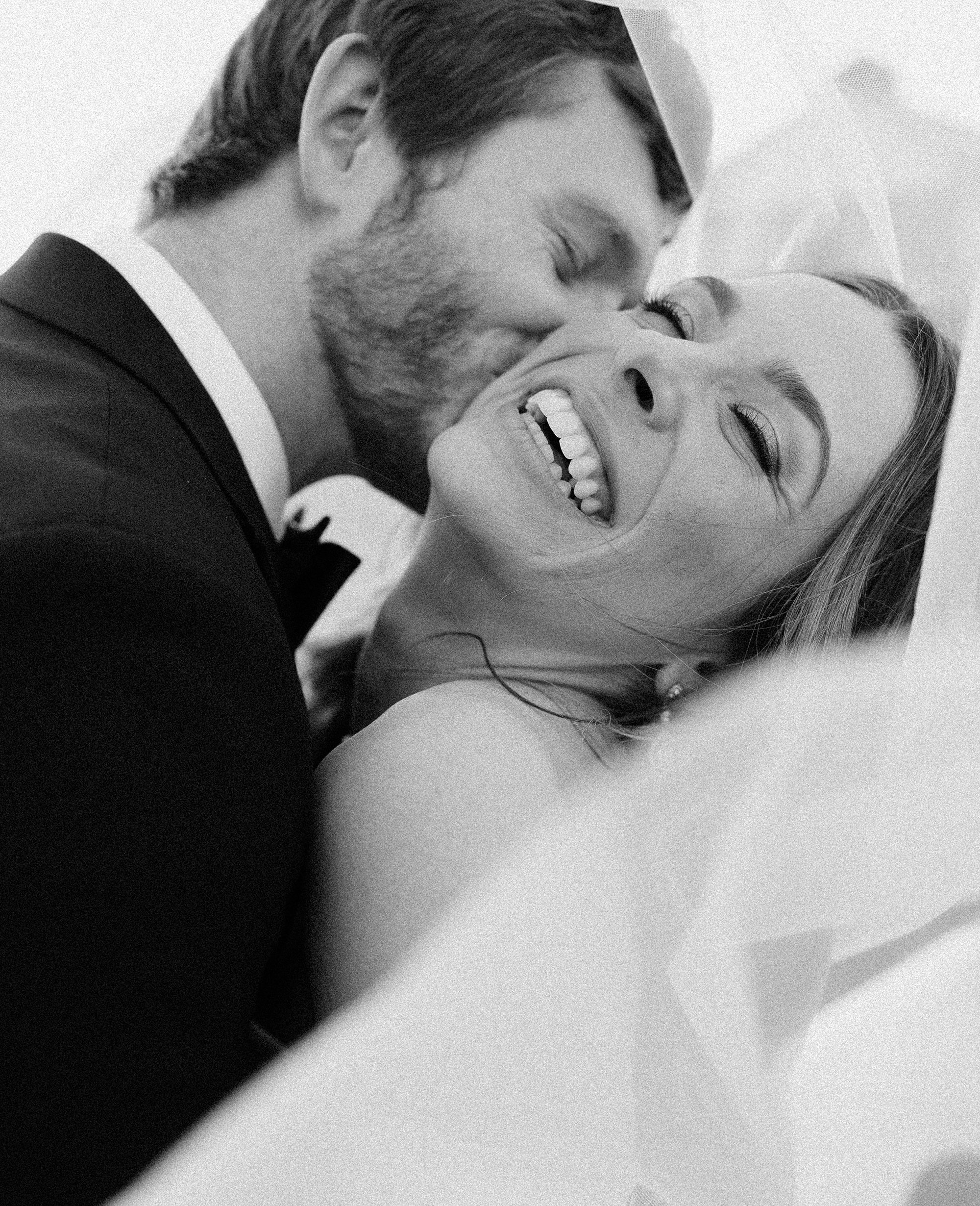 The groom kisses the brides cheek as she laughs at their wedding at venue Deep In The Heart Farms in Brenham, Texas