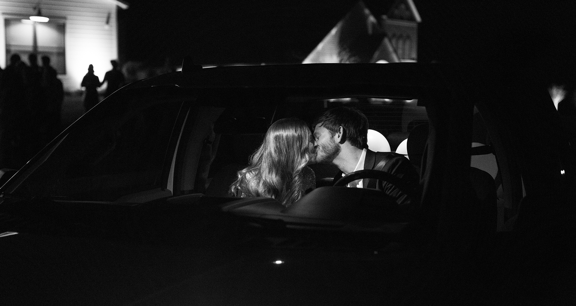 The bride and groom kiss in the car as they drive away from their wedding.