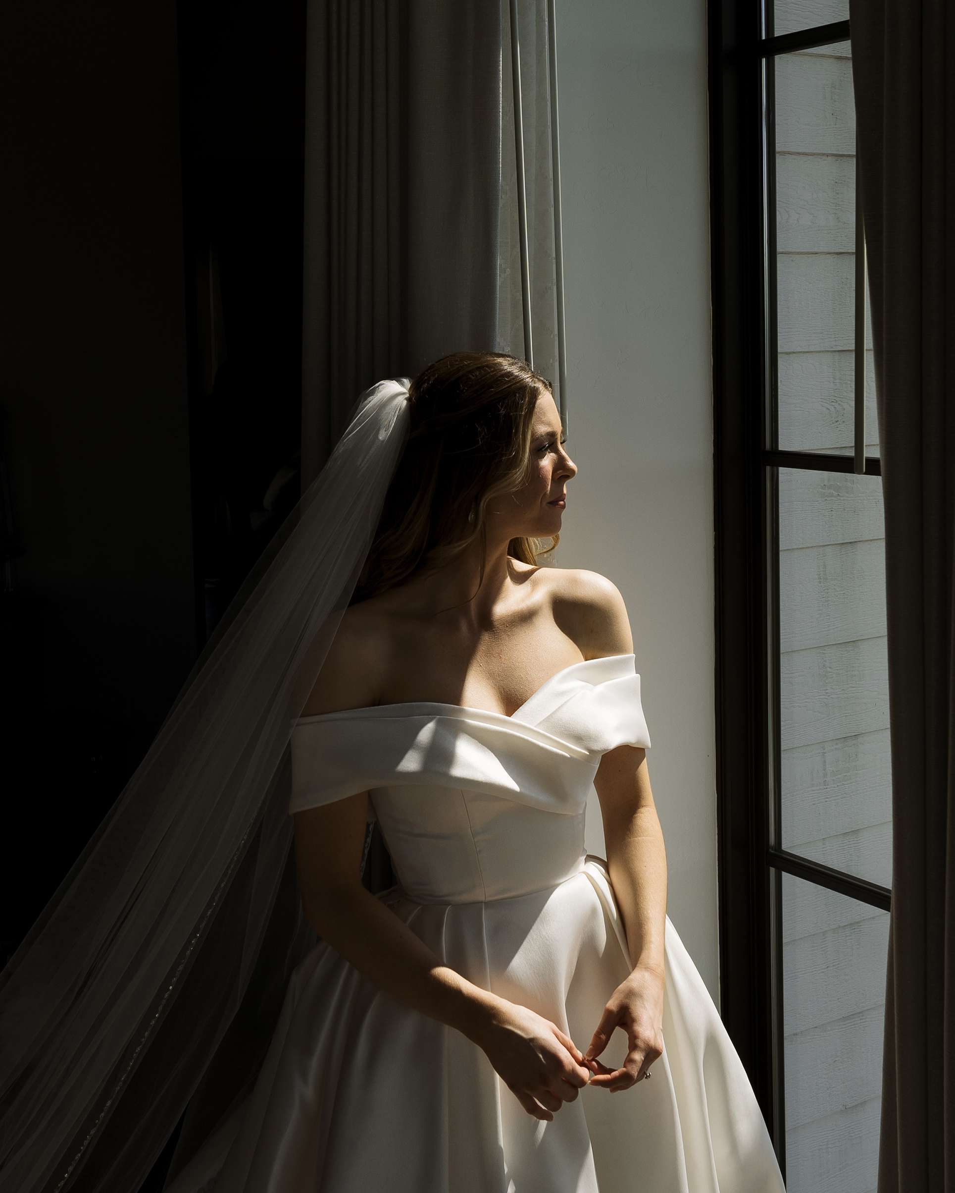 The bride is looking out the window in her wedding gown.