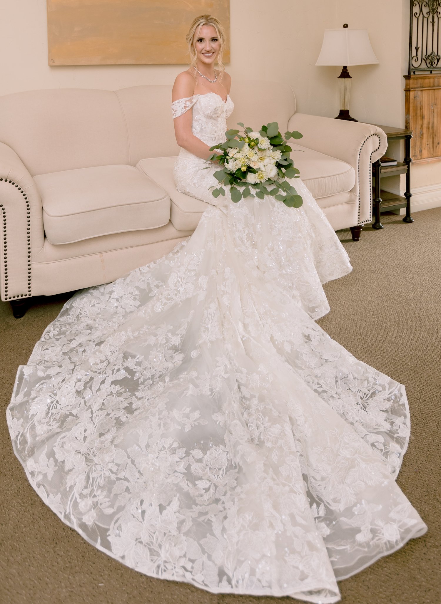 The bride is in her wedding dress sitting on a couch.
