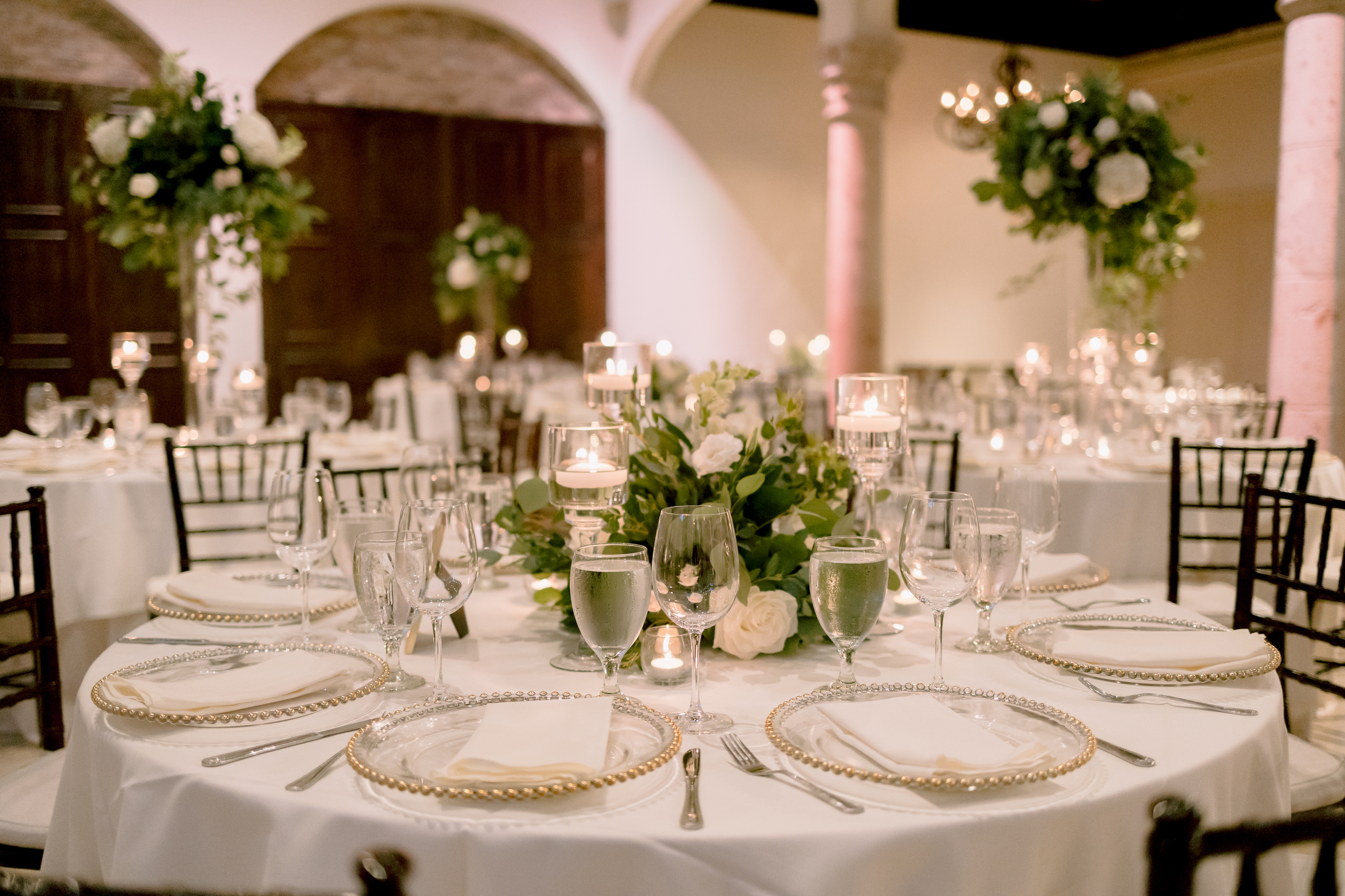 The reception tables have greenery centerpieces with white roses.