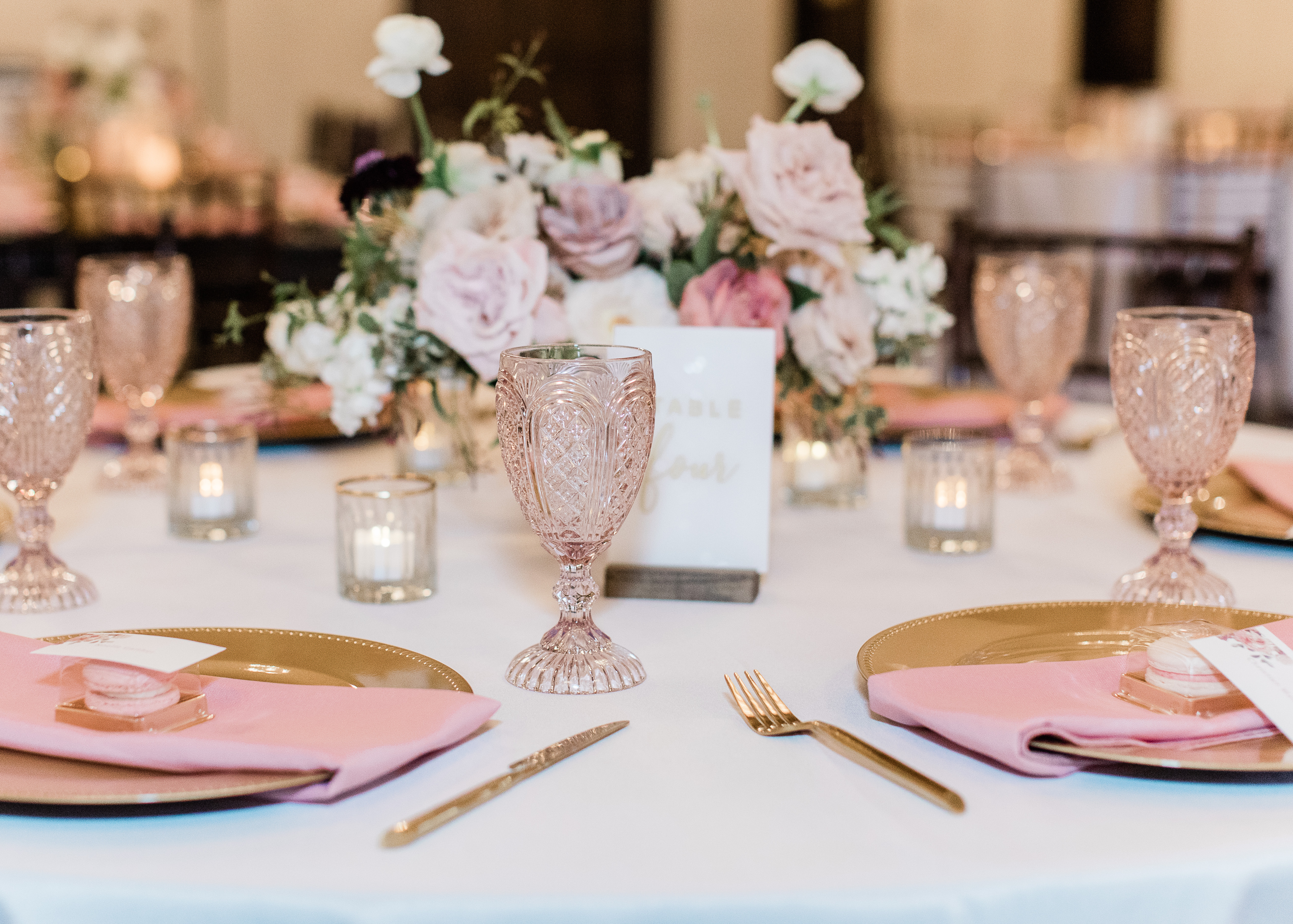 Table setting with gold chargers, pink napkins, pink glassware and fresh florals at a Texas hill country wedding reception at wedding venue,Ma Maison.