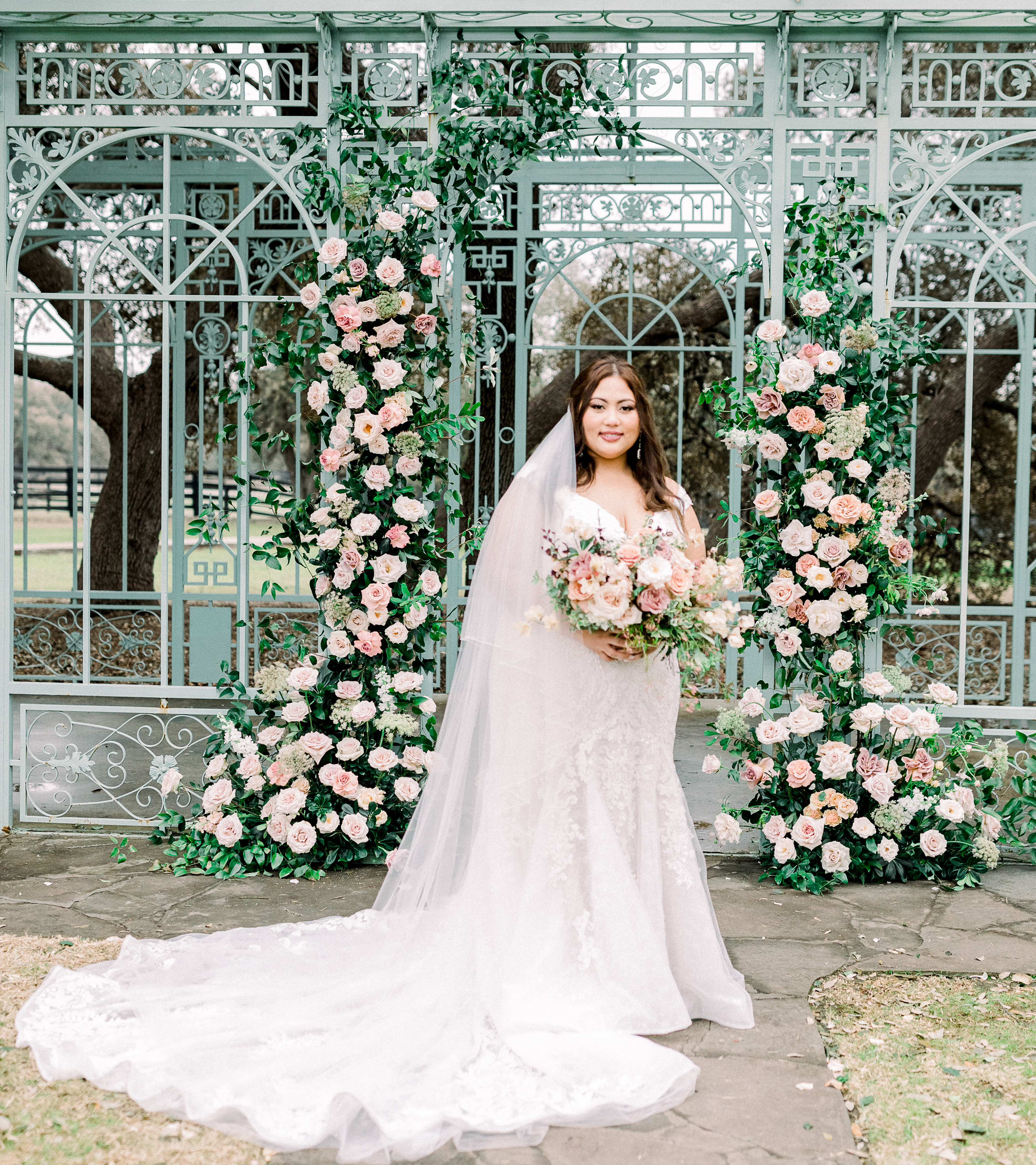 Bride holding fresh bouquet of pink, cream and white florals in front of an antique french gazebo at her outdoor wedding ceremony in Dripping Springs, Texas. 