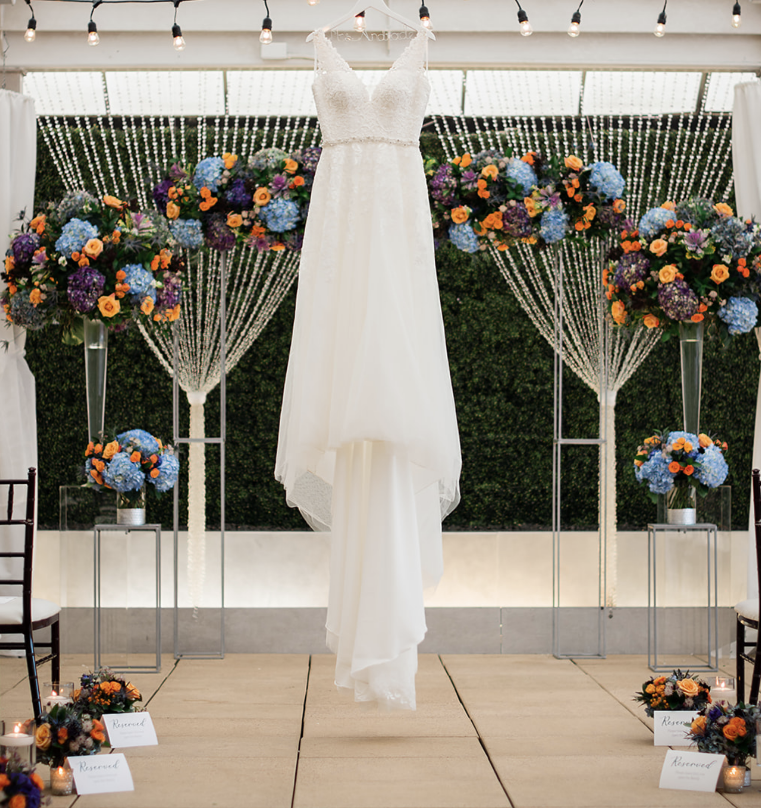The bride's wedding dress hangs in the front of the altar, which is decorated for the whimsical jewel-toned wedding.