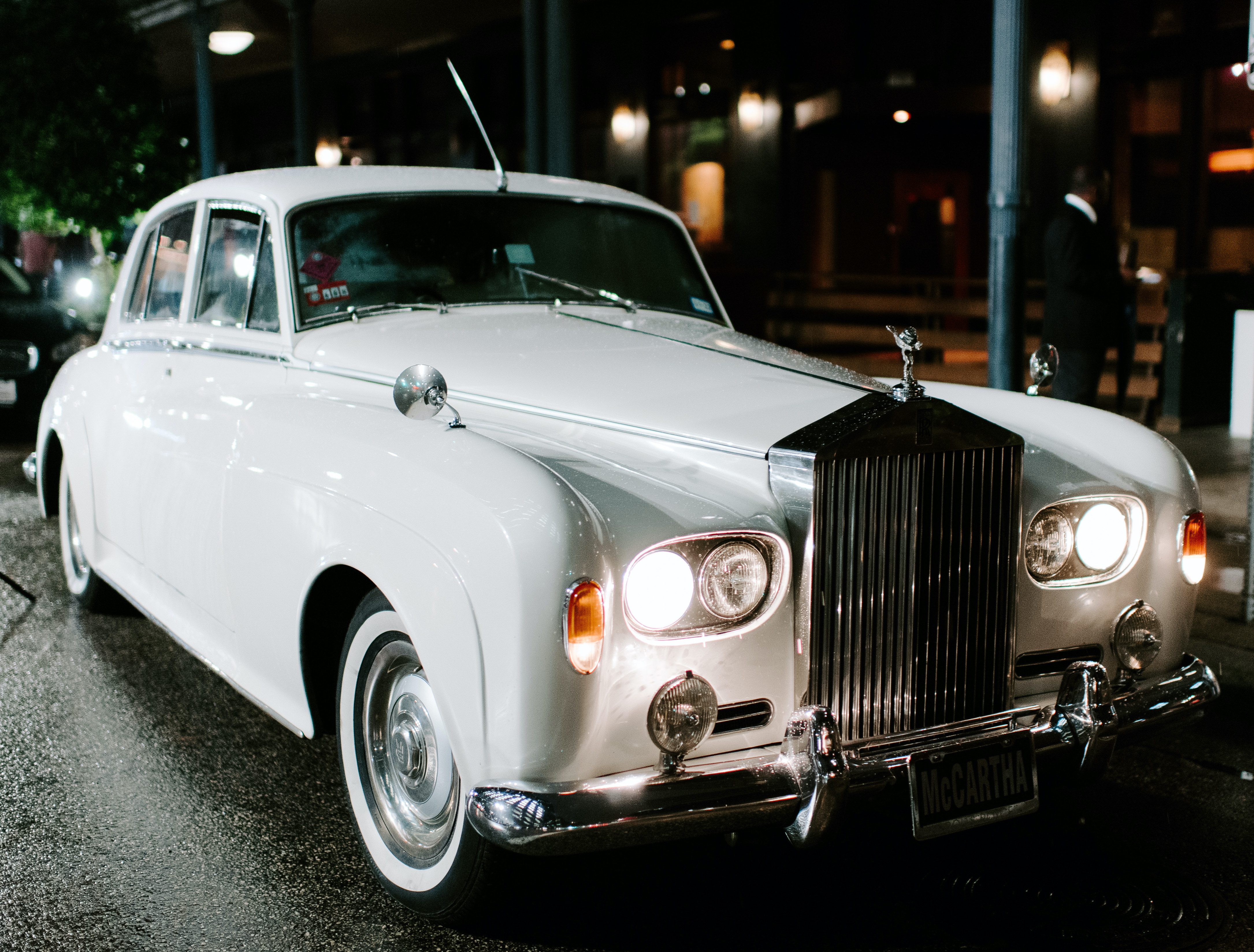 A white Rolls Royce is parked outside for the bride and groom.