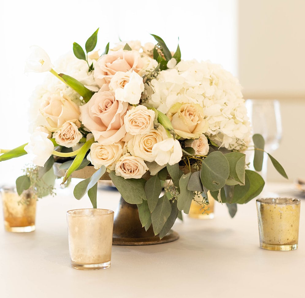 Bouquet of roses and hydrangea in a gold floral container with four mercury glass candle votives on a table in the Kendall Halle at The Kendall Hill Country Inn in Boerne, TX. 