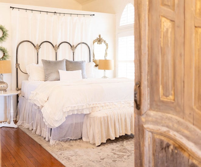 Interior of guest suite with queen size bed with ruffled white duvet, wood floors and two white wood nightstands with silver lamps at The Kendall Hill Country Inn.