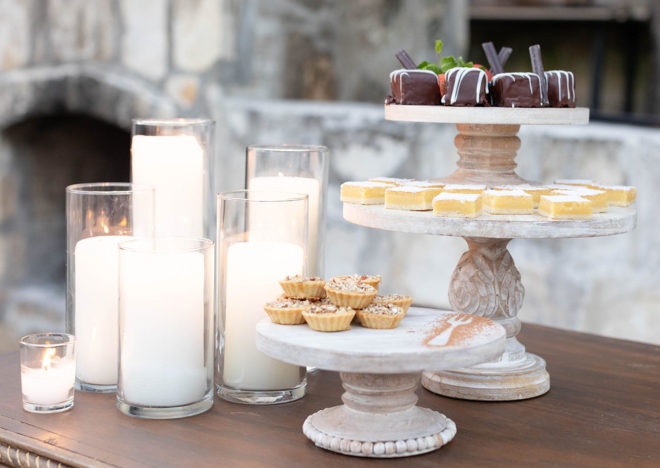 Outdoor table set with white washed wood cake platters with miniature desserts and five glass candleholders at The Kendall Hill Country Inn. 