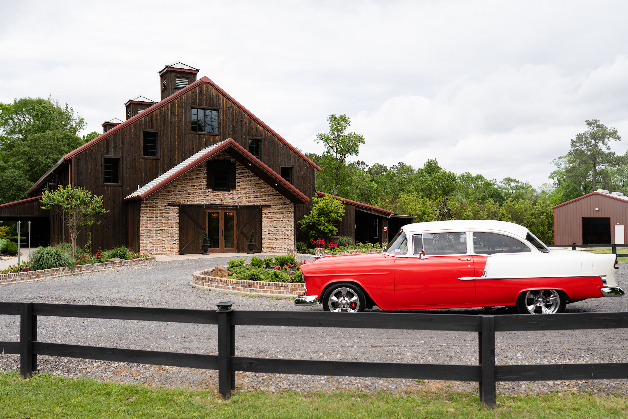 A classic red car is parked in front of The Carriage House, a big wooden barn reception space, before the burgundy wedding.