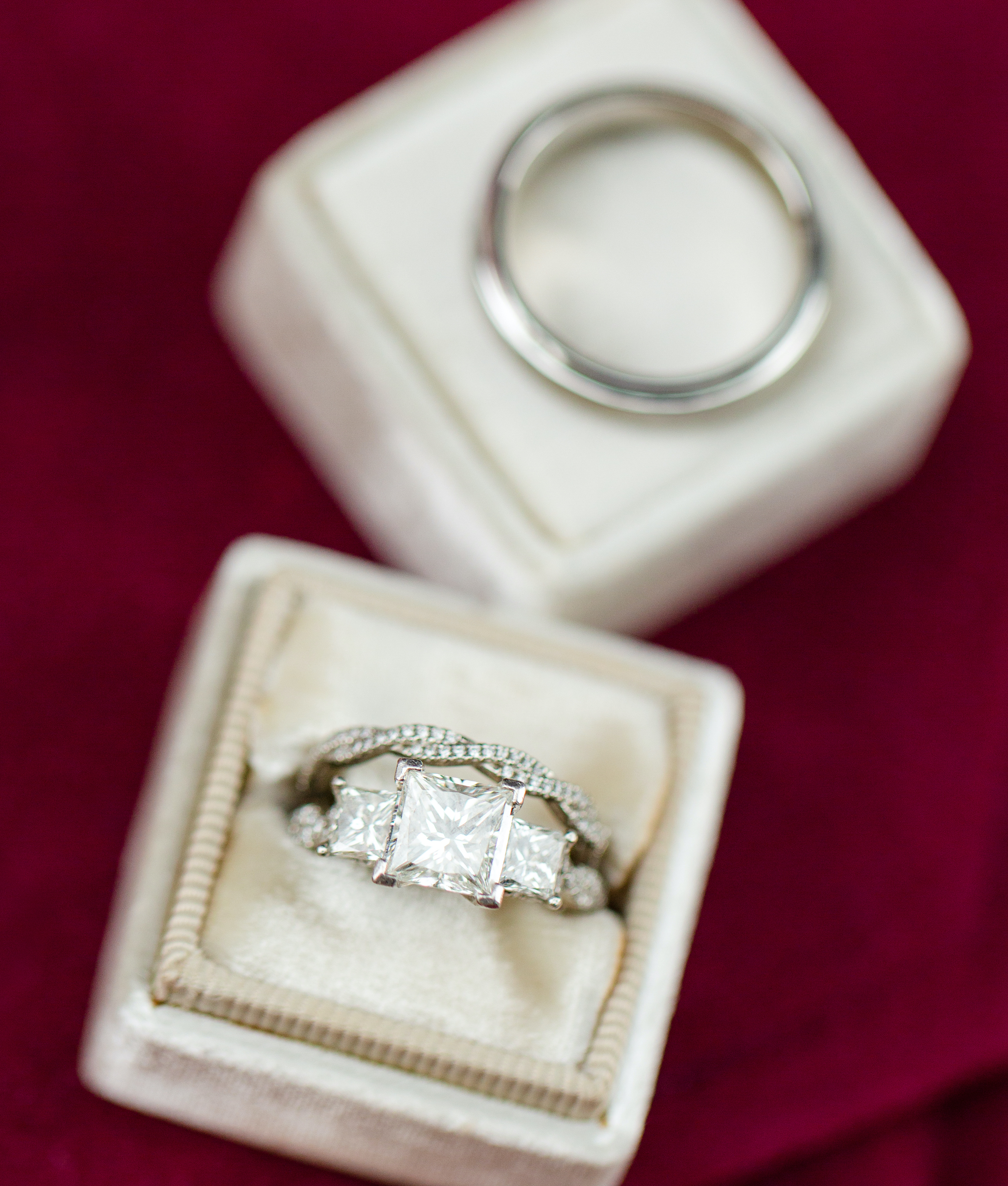 The bride's engagement ring is on a burgundy background and has square shaped diamonds.