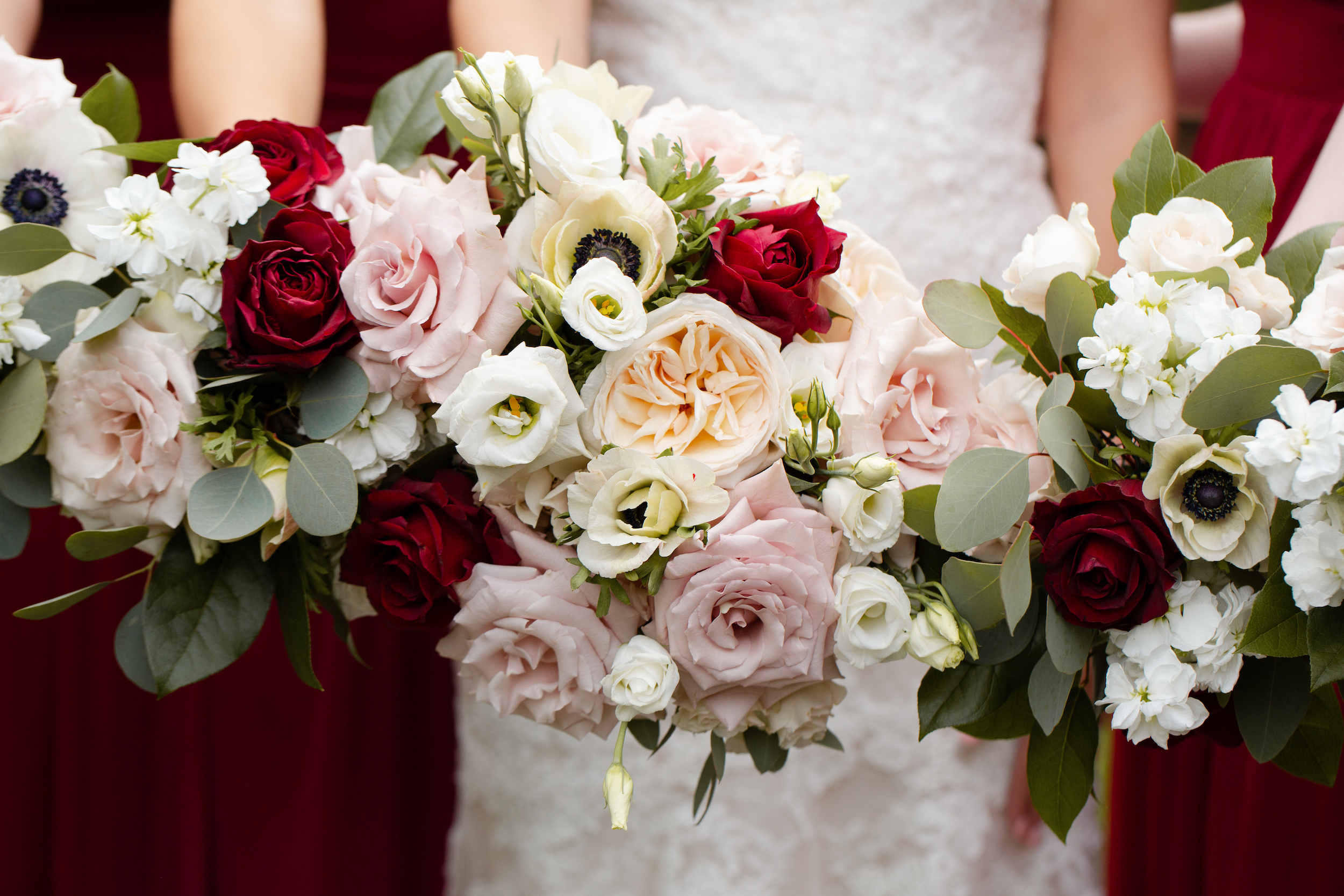 The bride and bridesmaids hold their blush and burgundy flower bouquets close to the camera lens.