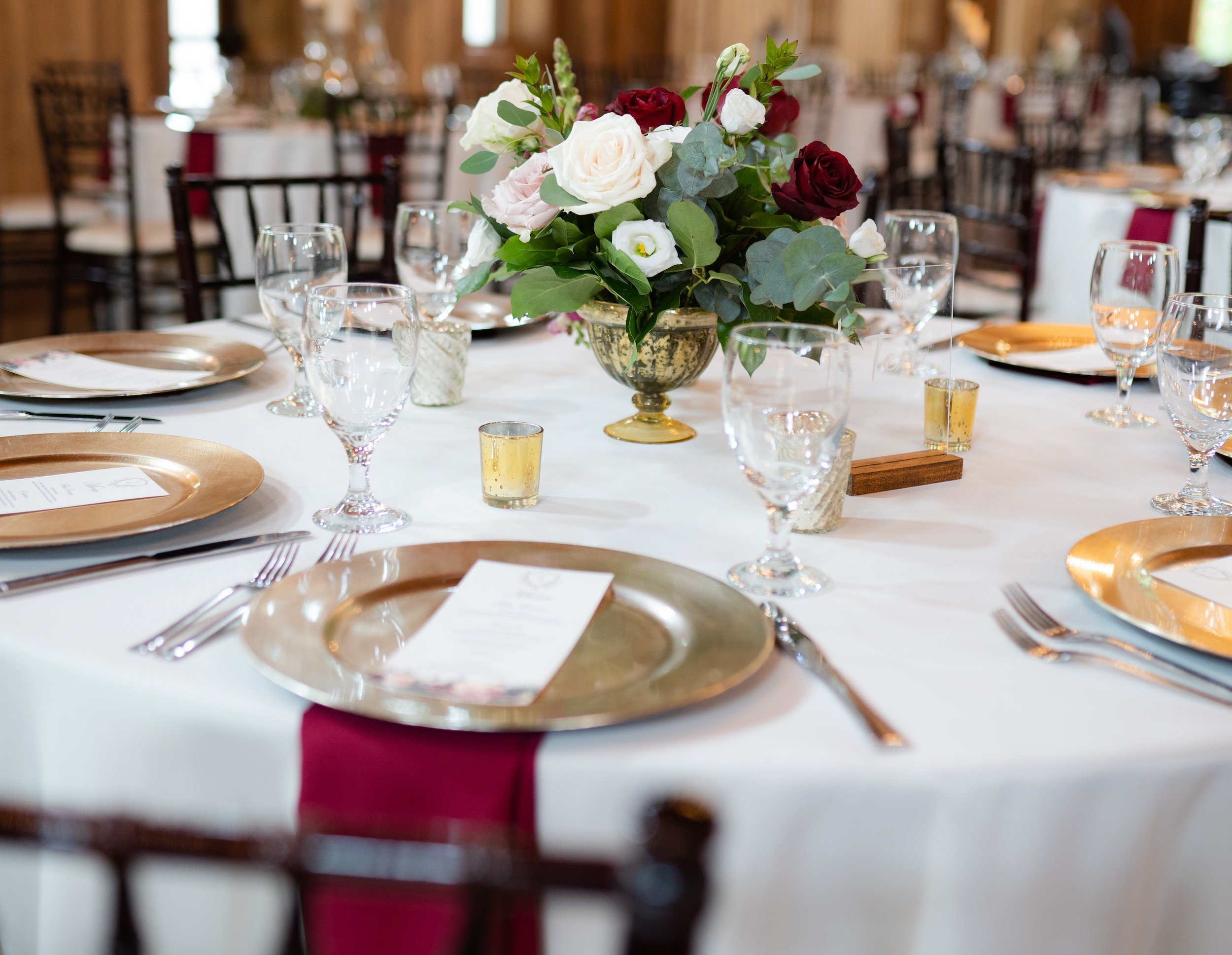 One of the reception tables is set up with gold and burgundy accents and floral centerpieces.