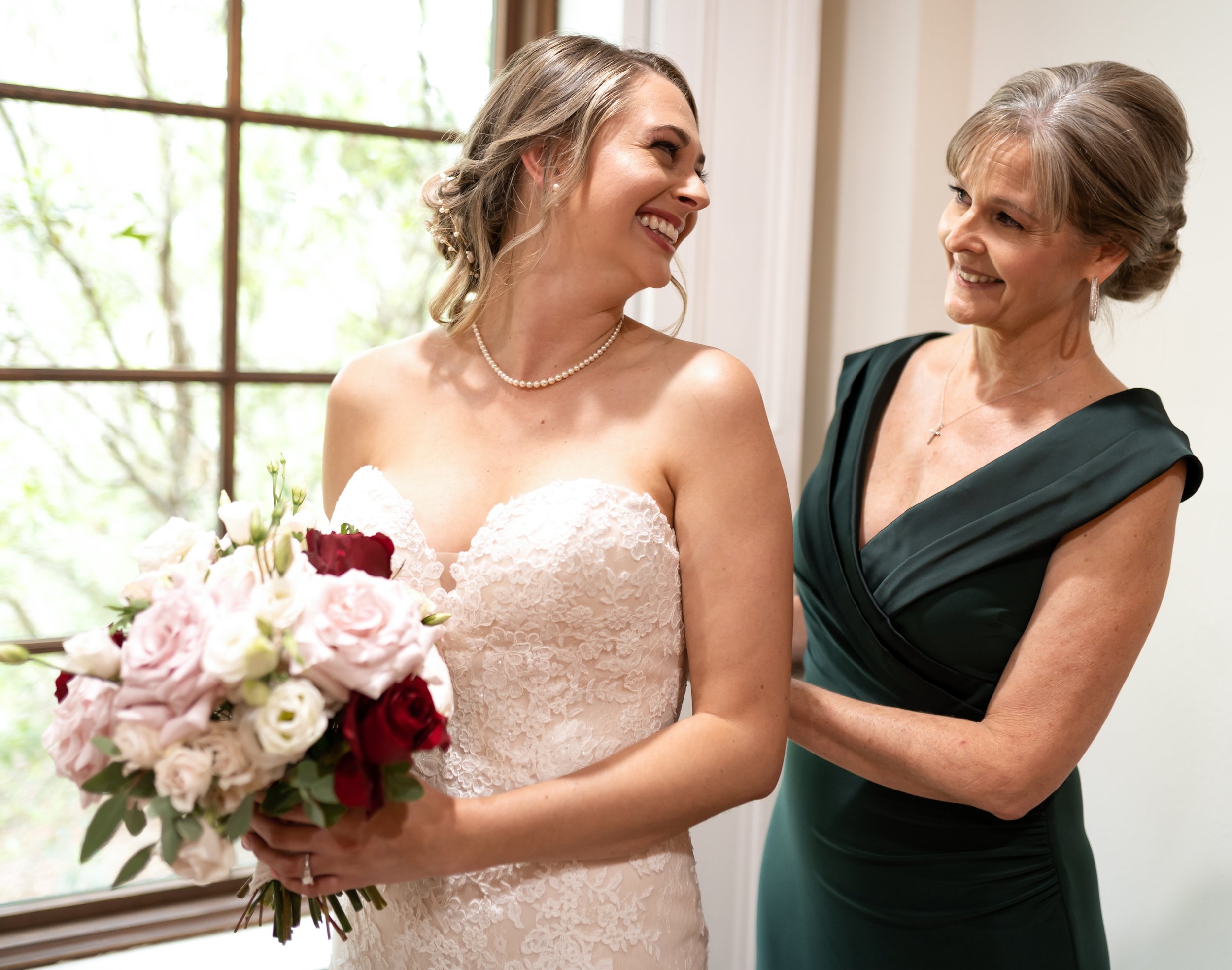 The bride smiles at her mom while she zips her gown at The Carriage House in Montgomery, TX.