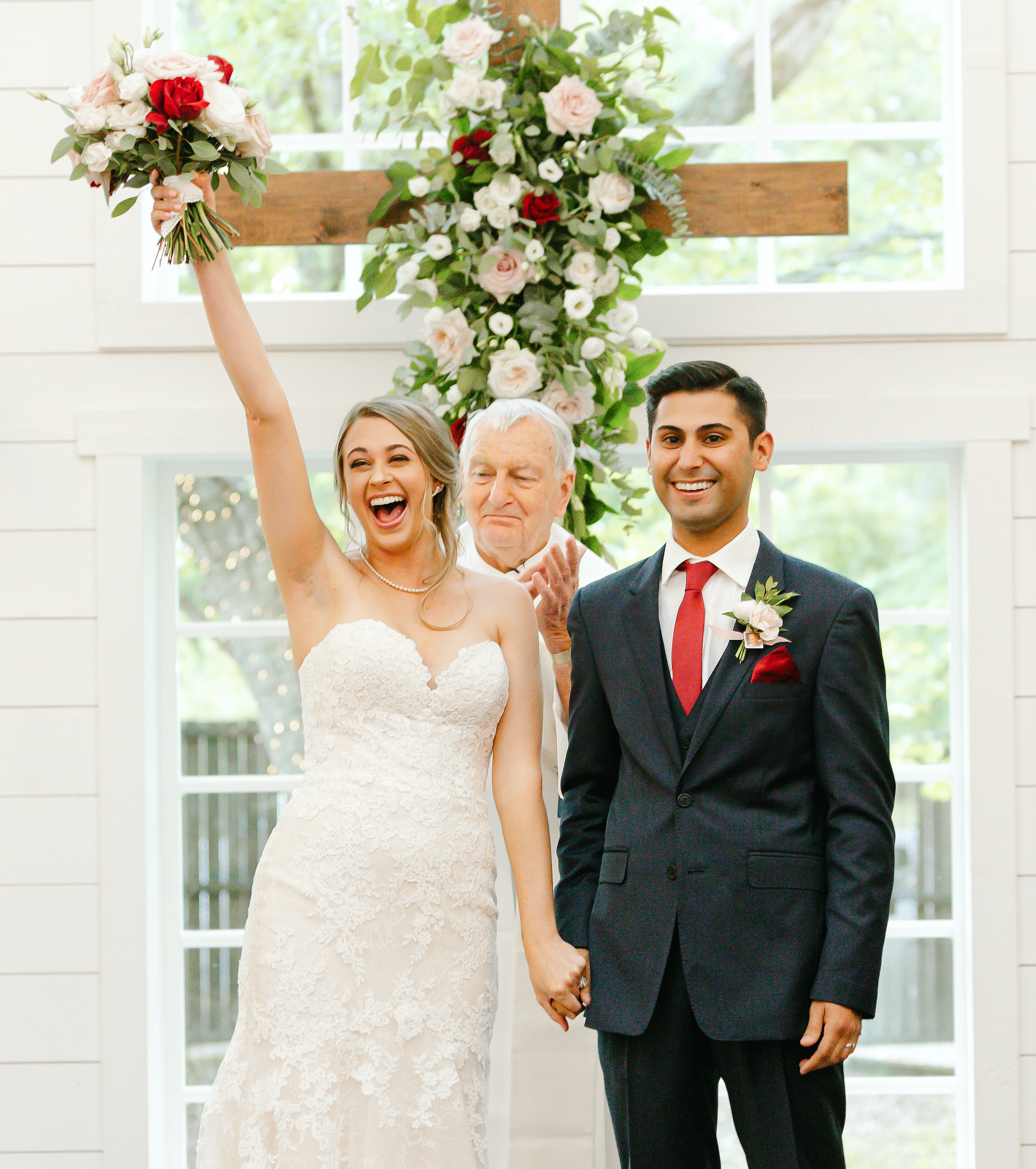 The bride holds her bouquet in the air and smiles, holding hands with her new husband at the altar in the chapel at The Carriage House in Montgomery, TX