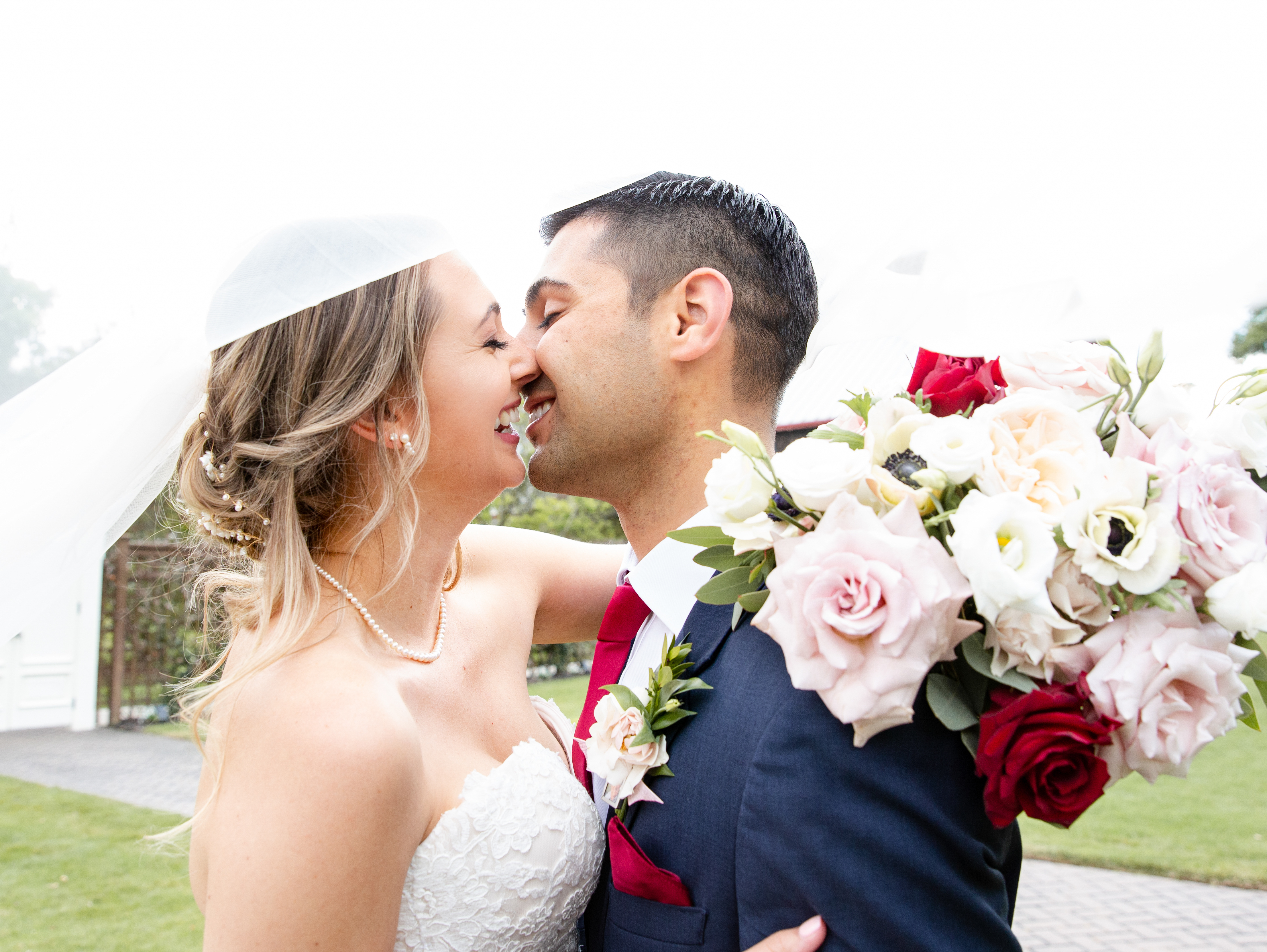 The bride has her arm wrapped around her husband, with her burgundy and blush bridal bouquet resting on his shoulder as she hugs him.