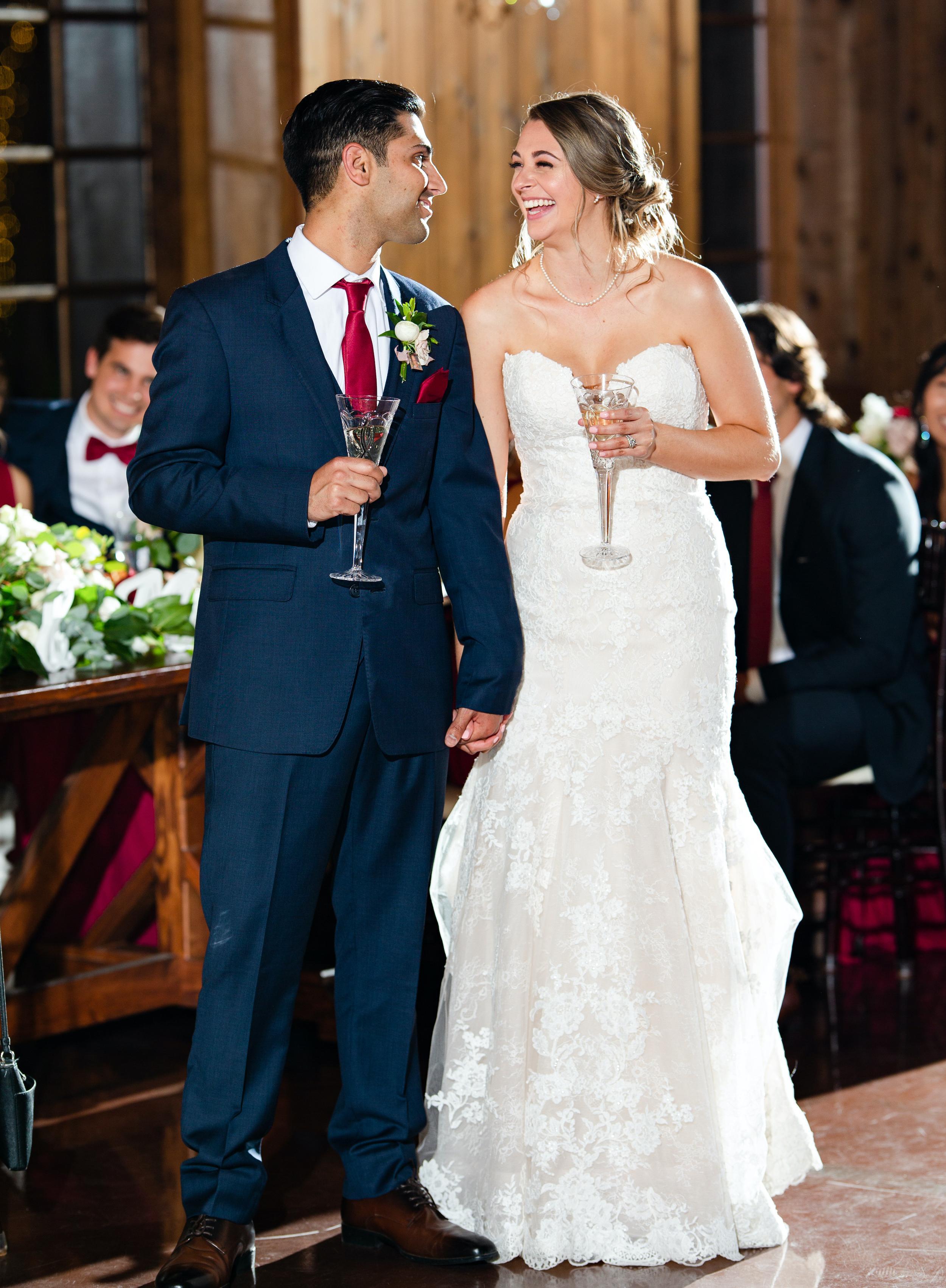 The bride and groom smile at each other at their reception while holding champagne glasses.