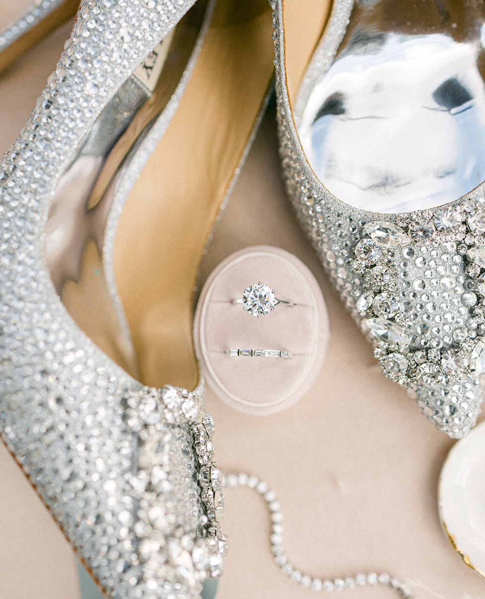The diamond engagement ring sits in between the bride's shoes, which were used for the ethereal wedding styled shoot.