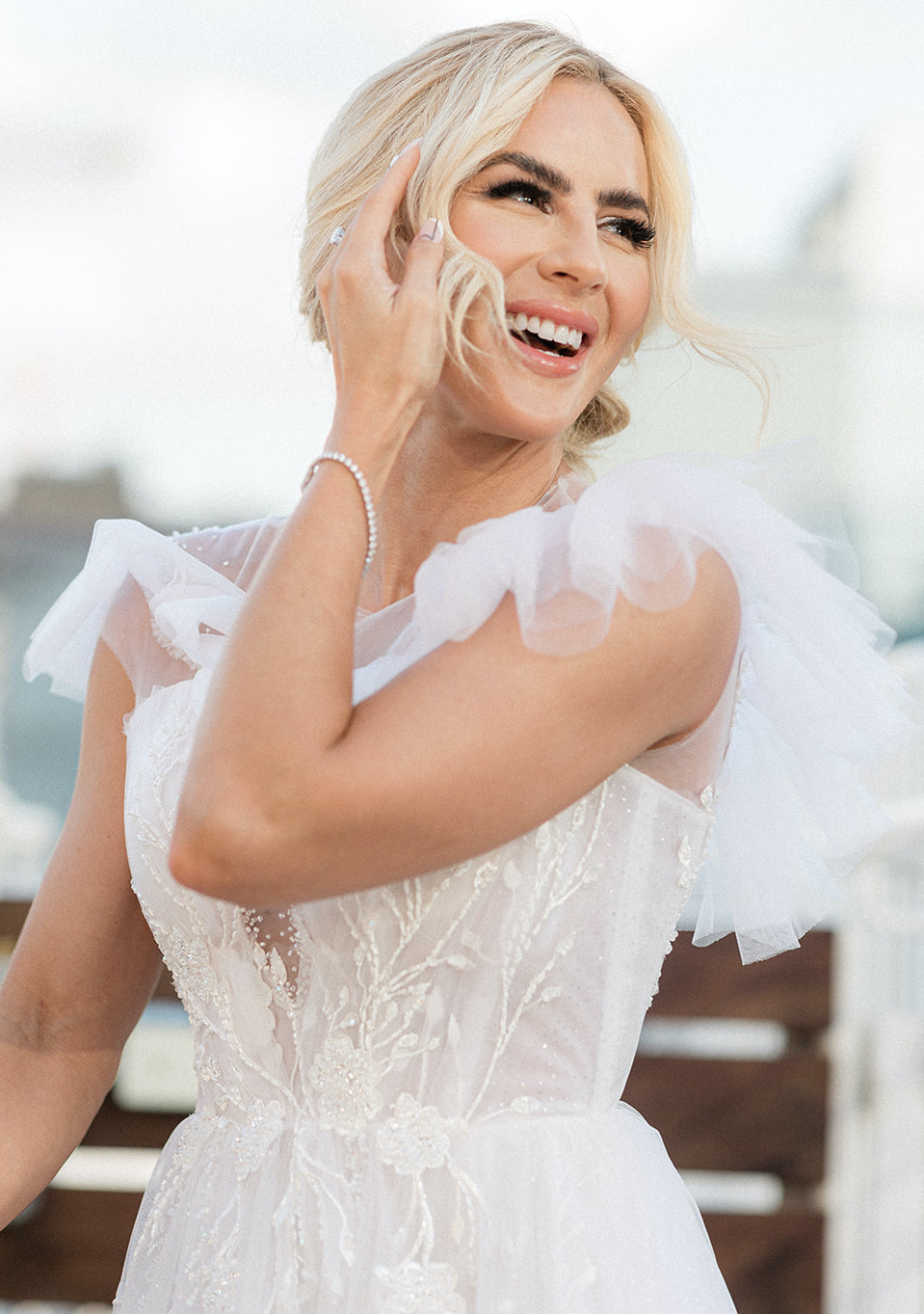 The bride looks to the sky laughing, while wearing a wedding gown with flowers and tulle detailing.