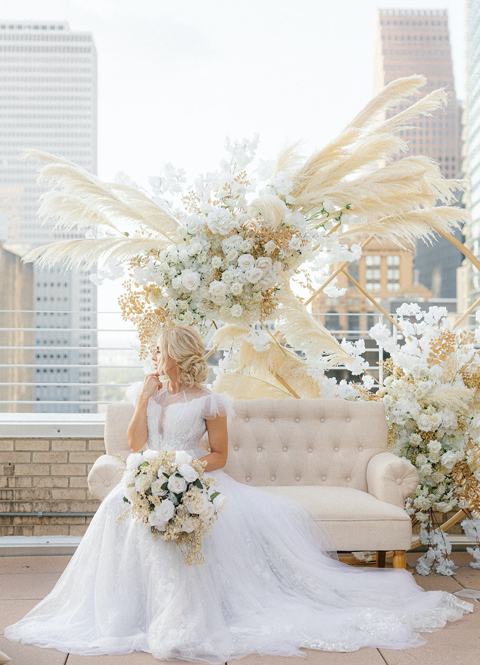 Bride is sitting on a chair decorated with bohemian flowers and pampas grass for the ethereal rooftop wedding styled shoot.