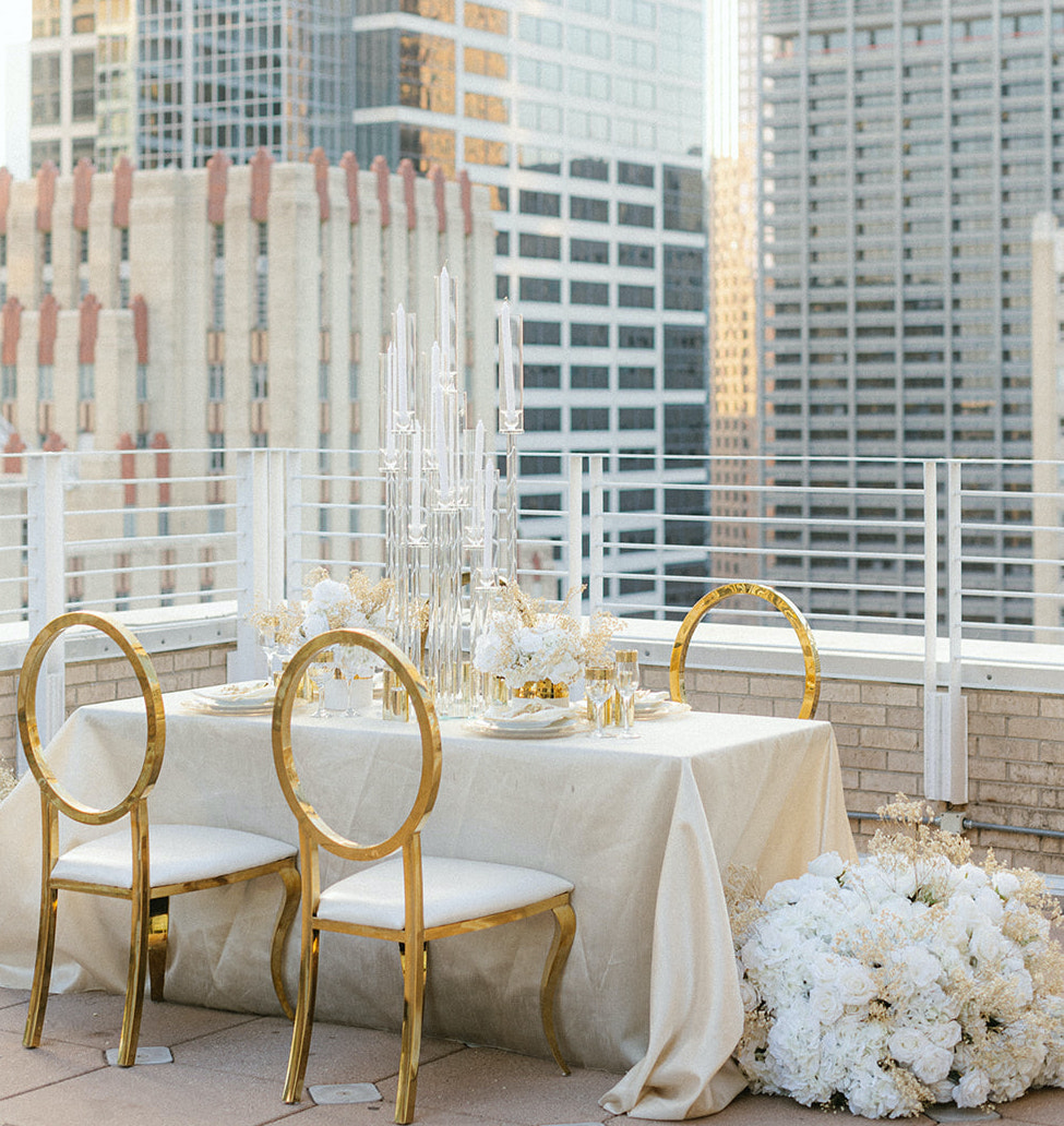 A photo of the table set-up for the ethereal rooftop wedding styled shoot. It has gold chairs and dinnerware, with flowers adorned on the side of the table.