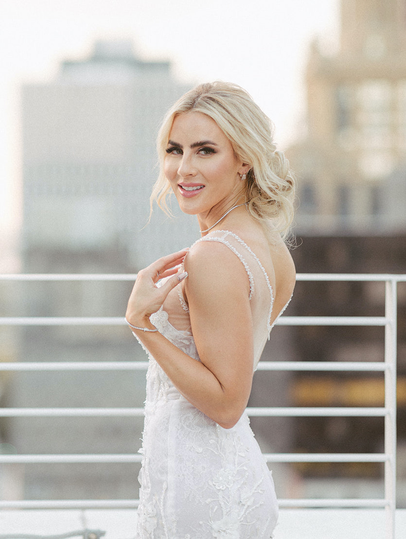The bride is turned and looking back at the camera smiling, for the ethereal rooftop wedding styled shoot.