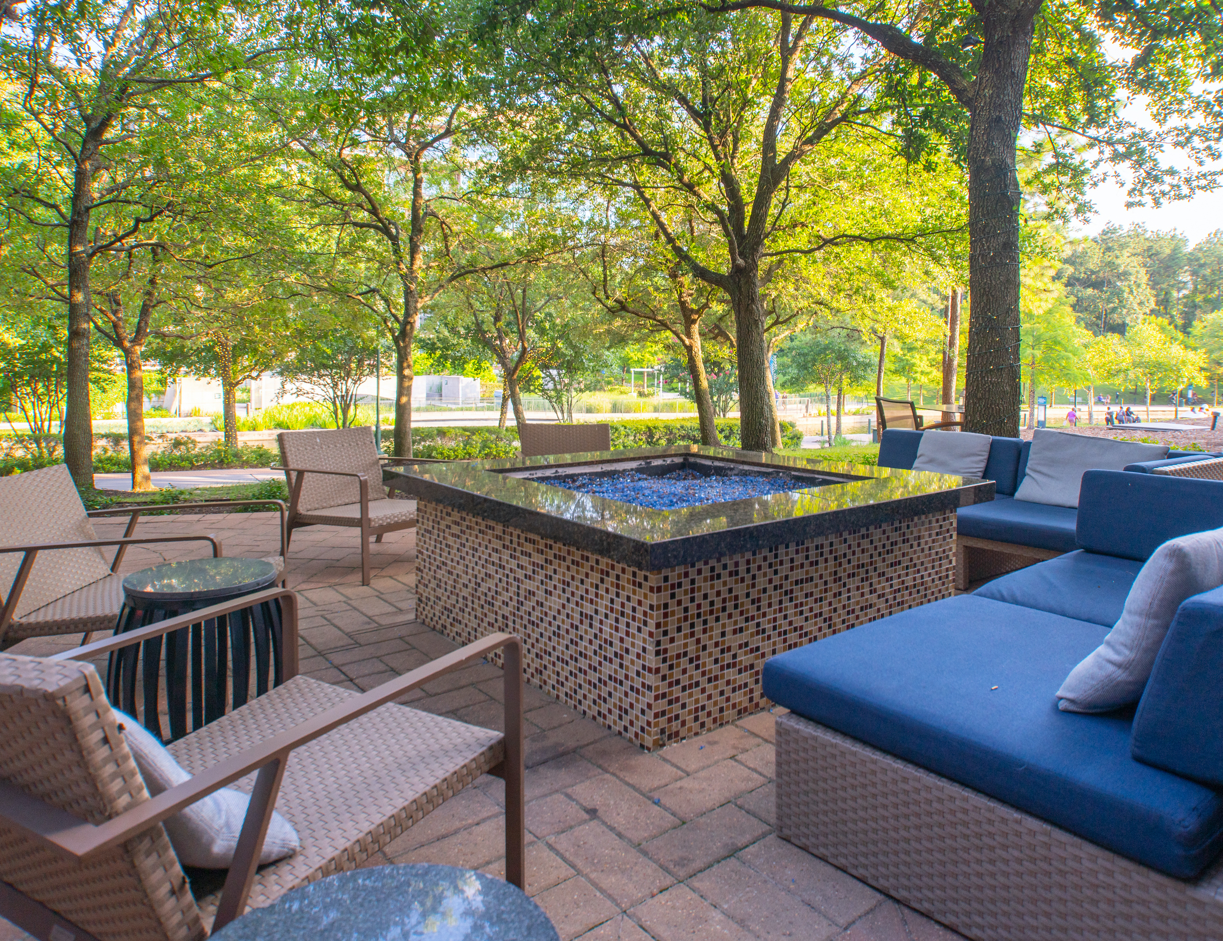 Blue-cushioned outdoor seating set on an outdoor patio with a fireplace in the center, both overlooking the trail and Woodlands Waterway canal at the a Marriott hotel in the Woodlands, TX.