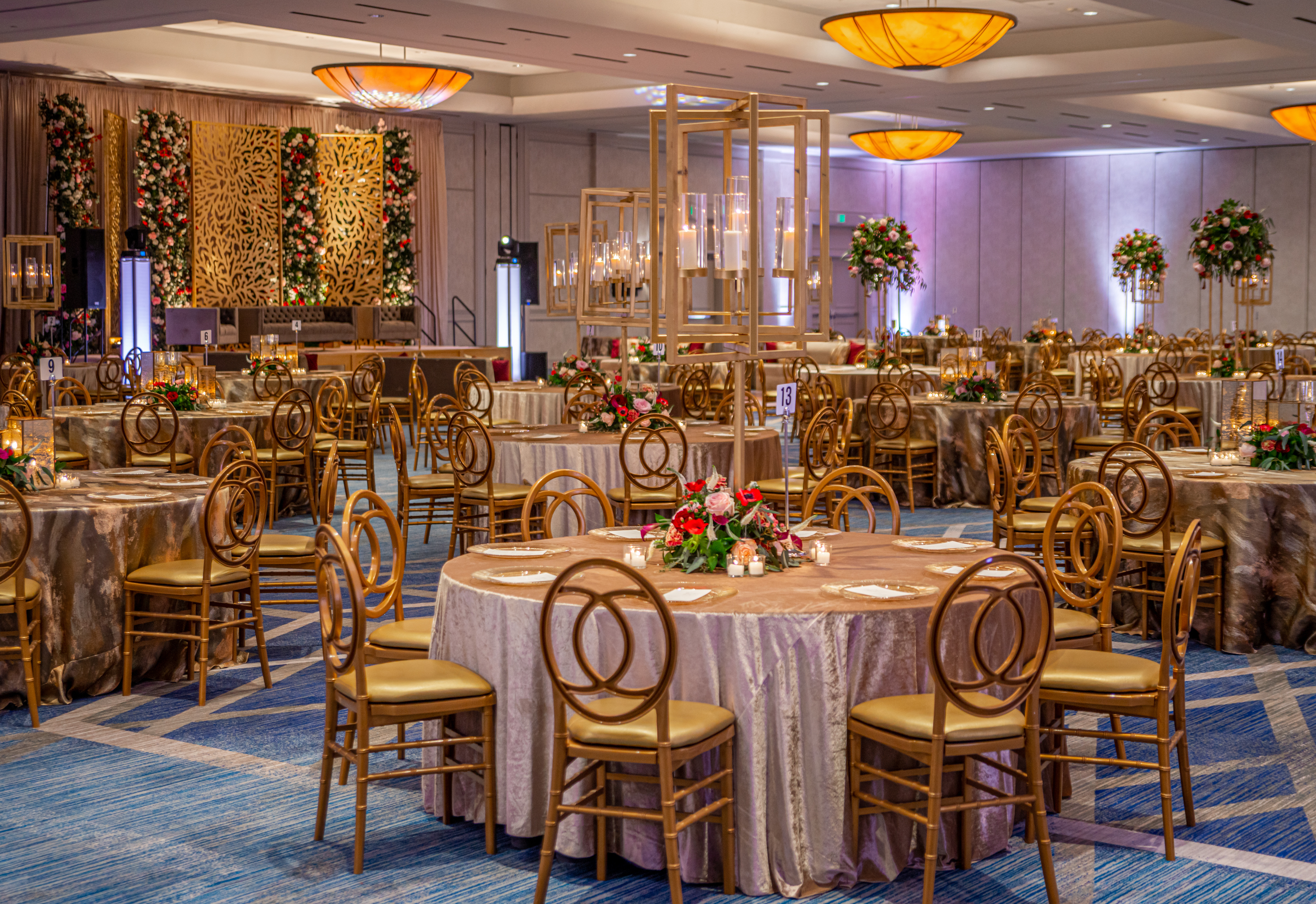 Ballroom at The Woodlands Waterway Marriott Hotel decorated with gold accents and red and pink flowers at a wedding reception. 
