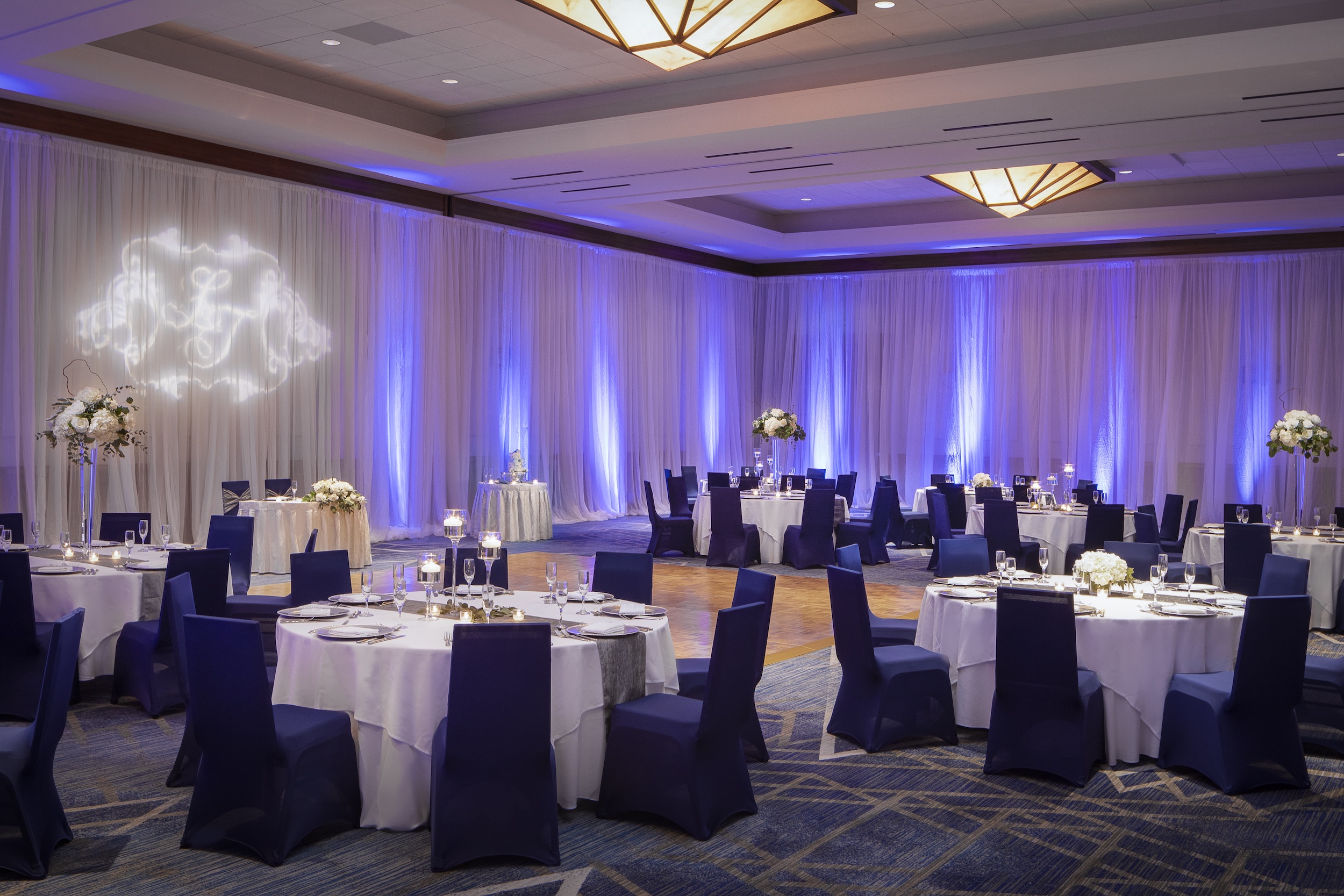 A wedding venue space at The Woodlands Waterway Marriott decorated with navy blue chairs, blue lighting, and white linens.
