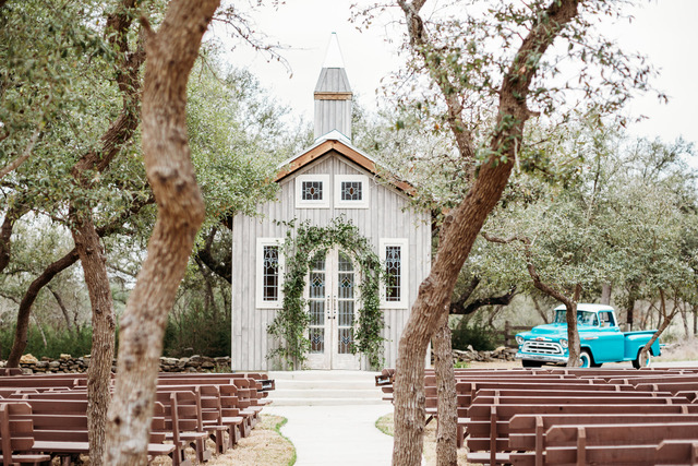 A little outdoor chapel with rows of pews and a turquoise vintage truck that are apart of a hill country wedding venue.