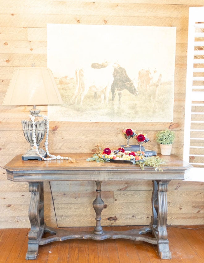 Wood table set with lamp, florals and metal tray with florals, nuts, cheese and grapes inside a guest suite at The Kendall. 