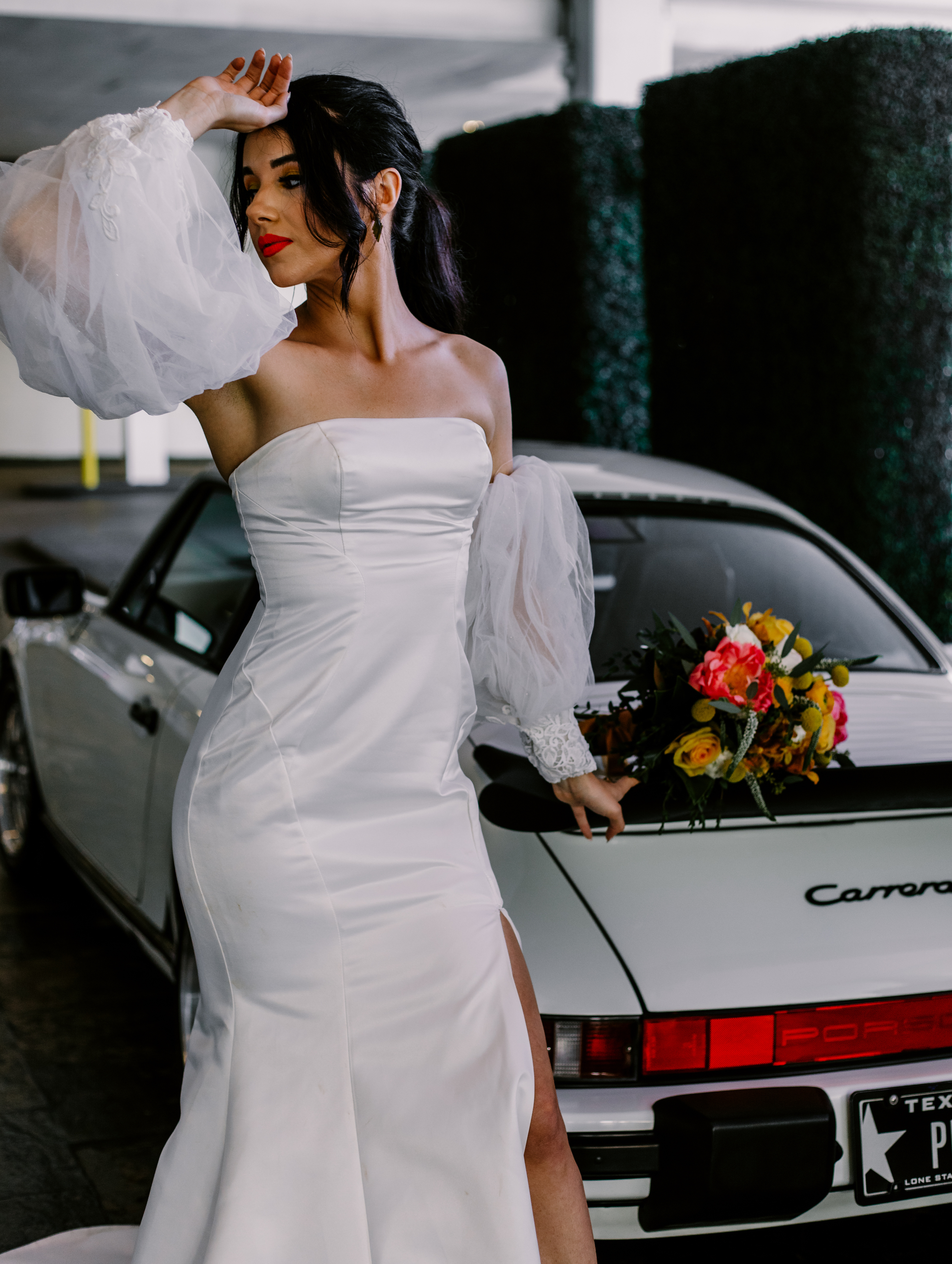 A bride poses next to a white vintage Porsche while her bridal bouquet is set on top of the trunk.