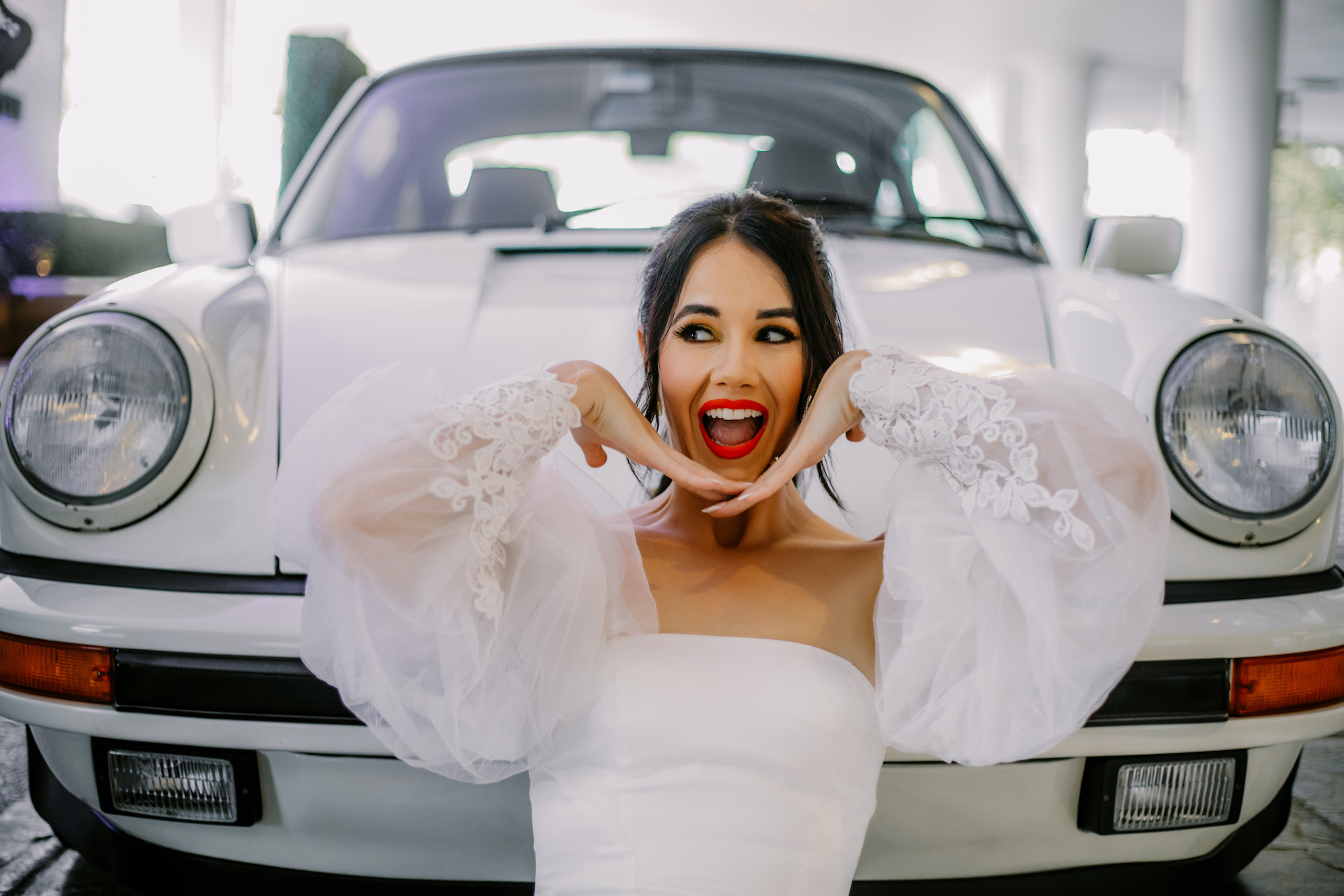 A bride poses while posing in front of a white 1987 Porsche 911 at The White Hotel. 