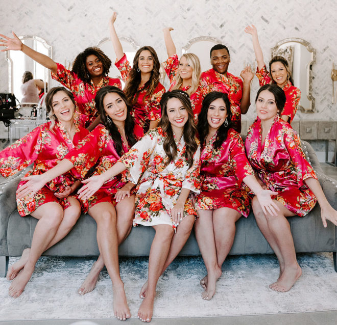 The bride sits with her bridesmaids as they all pose in bright red silky robes, getting ready for the bride's wedding day.