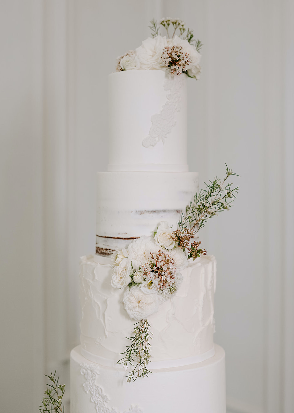 The wedding cake has ivory textured frosting and dainty whimsical flowers along each tier at a wedding reception at The Peach Orchard Venue. 