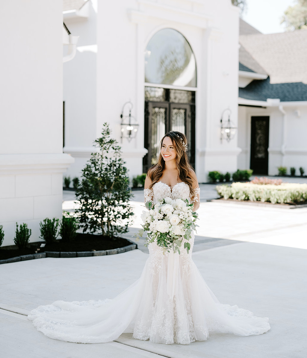 The bride stands outside The Peach Orchard holding her bridal bouquet, which is full of lush greenery and ivory flowers.